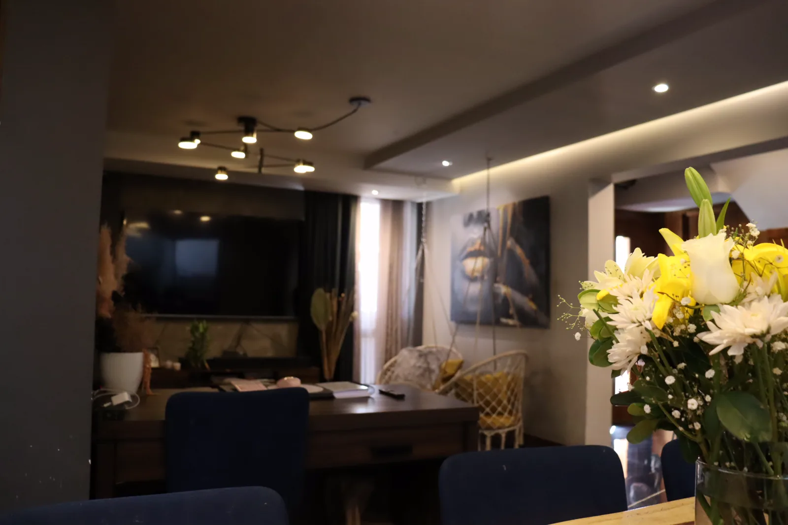 Sala y comedor bajo un plafón con luz indirecta y una lámpara de brazos negra.