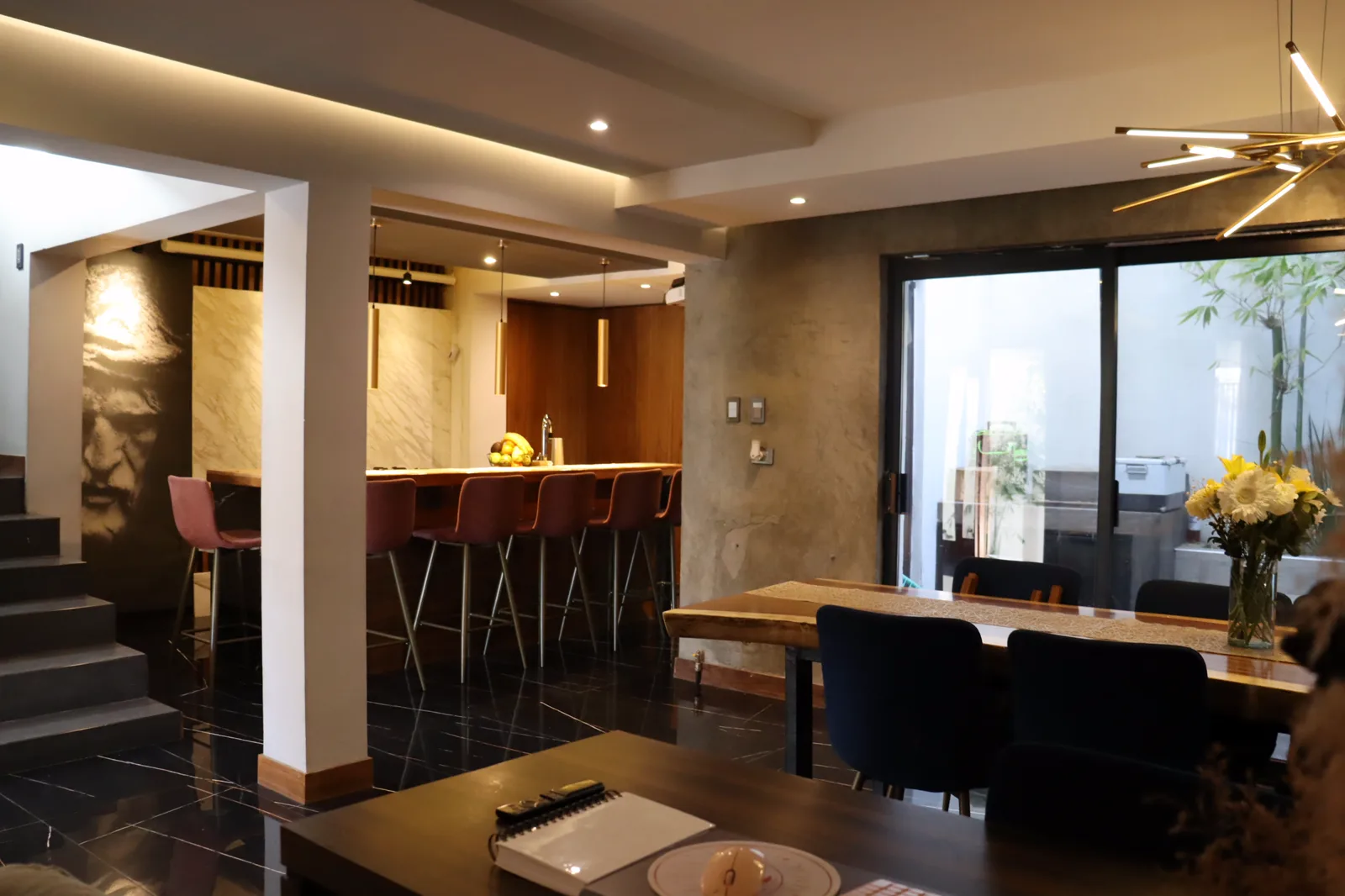 Planta baja abierta, con el comedor, la barra de la cocina y el ventanal hacia el patio con vegetación.