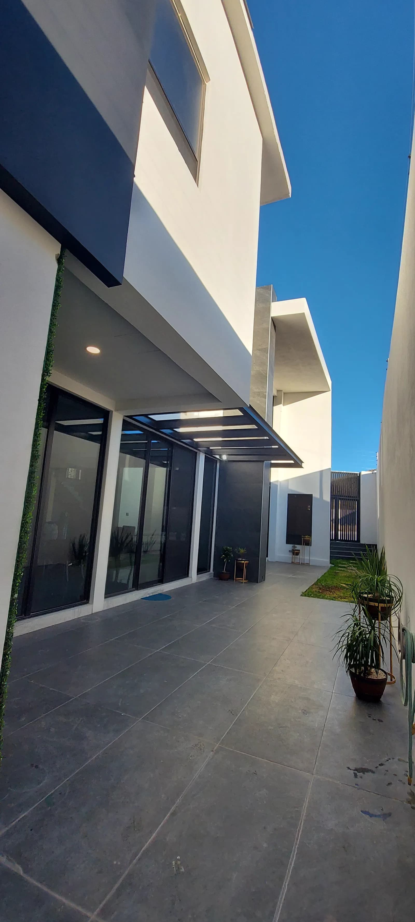 Patio lateral con piso de porcelanato gris y el ventanal corrido de la planta baja.