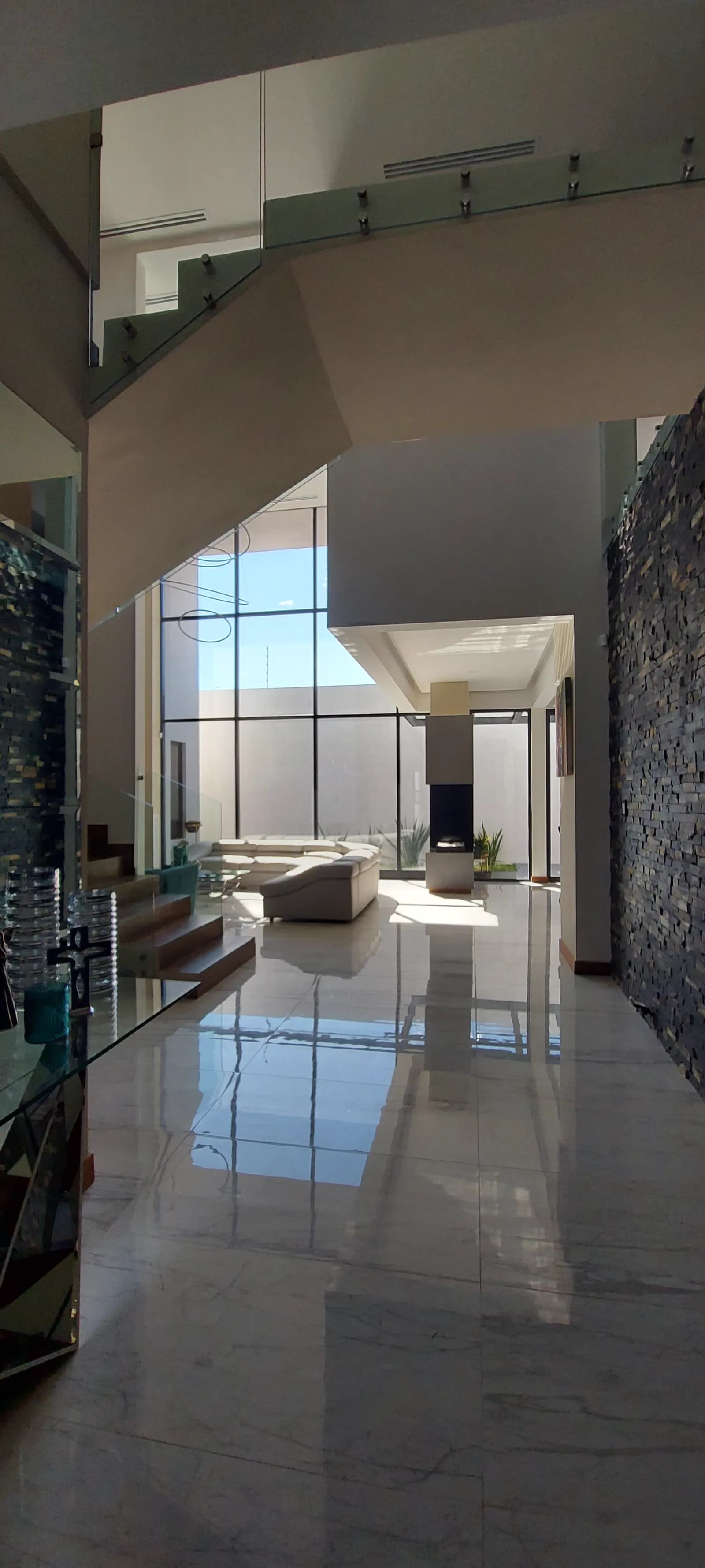 Pasillo interior con piso de mármol claro, barandal de cristal y la sala al fondo.
