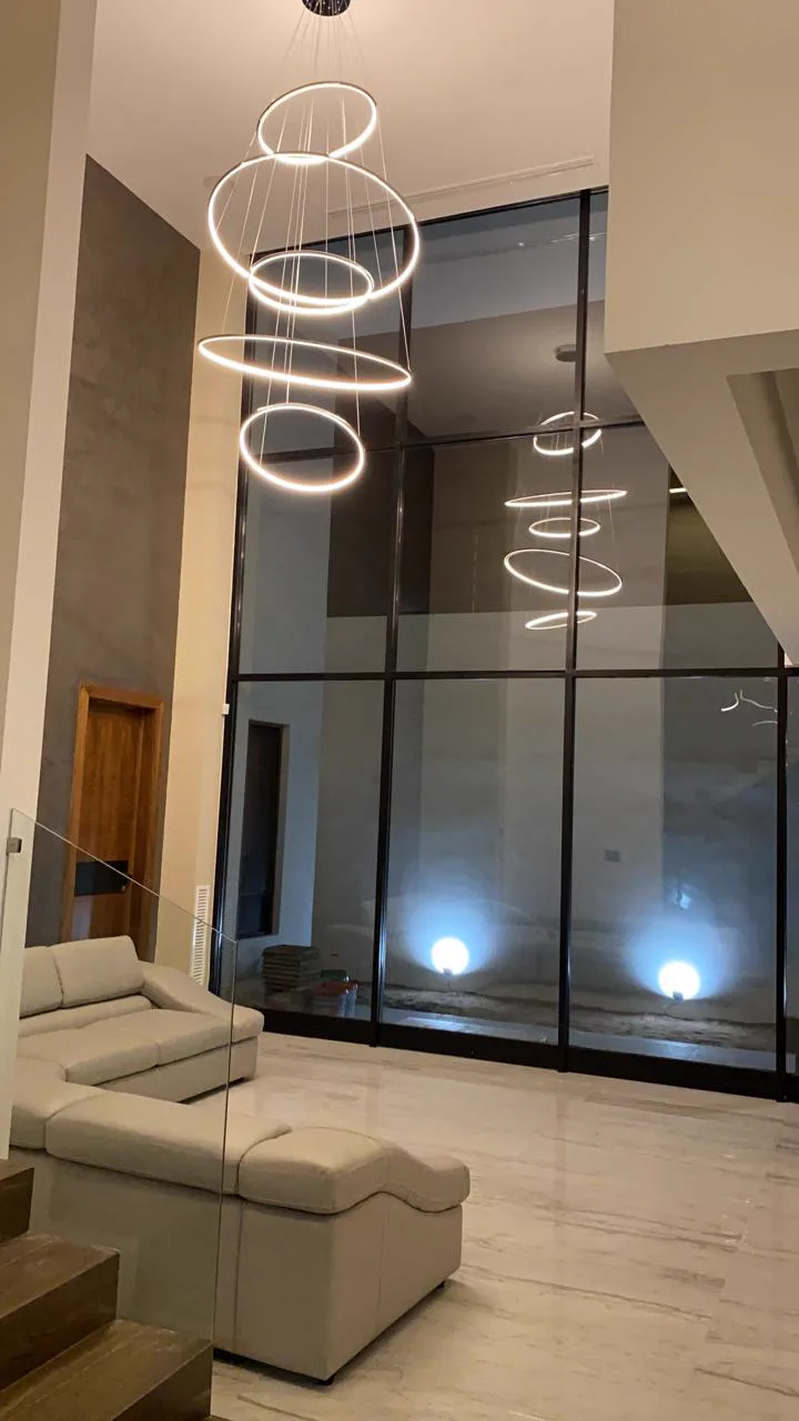 Lámparas de anillos iluminadas en la doble altura, sobre la sala con sillones claros.