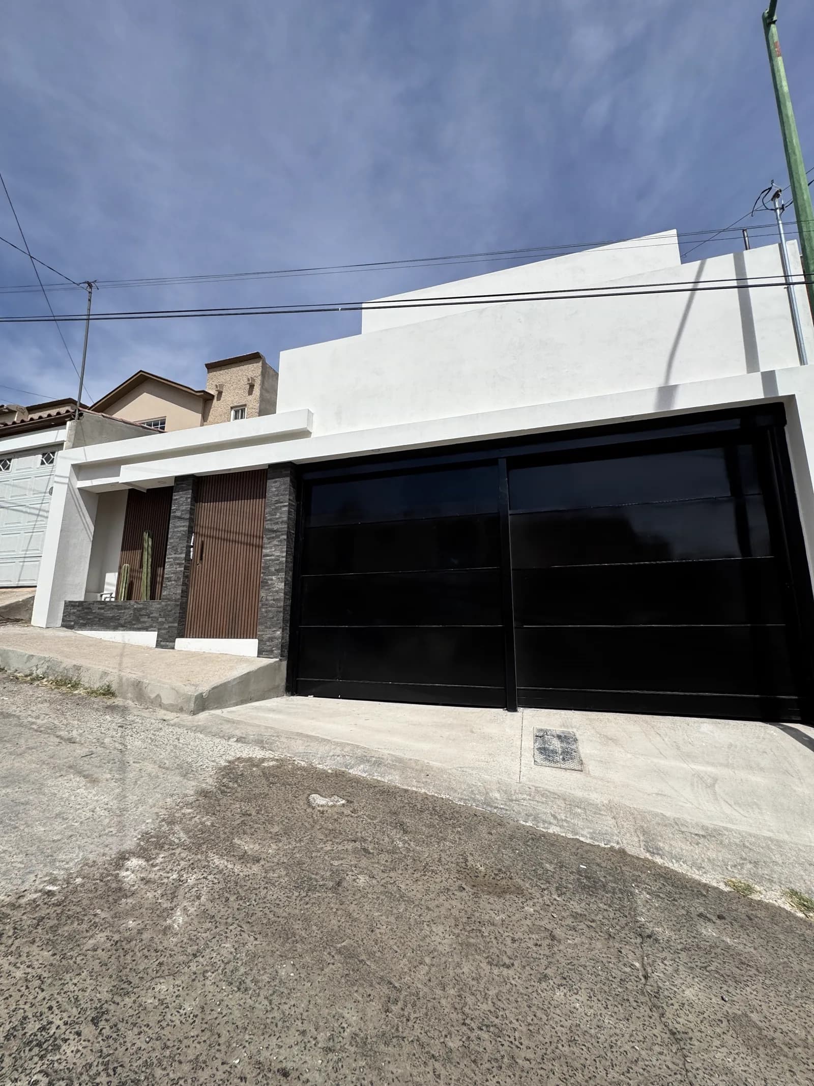 Fachada terminada de Casa Barrancas 02, con el volumen blanco, los listones de madera y el portón de cristal negro de la cochera.