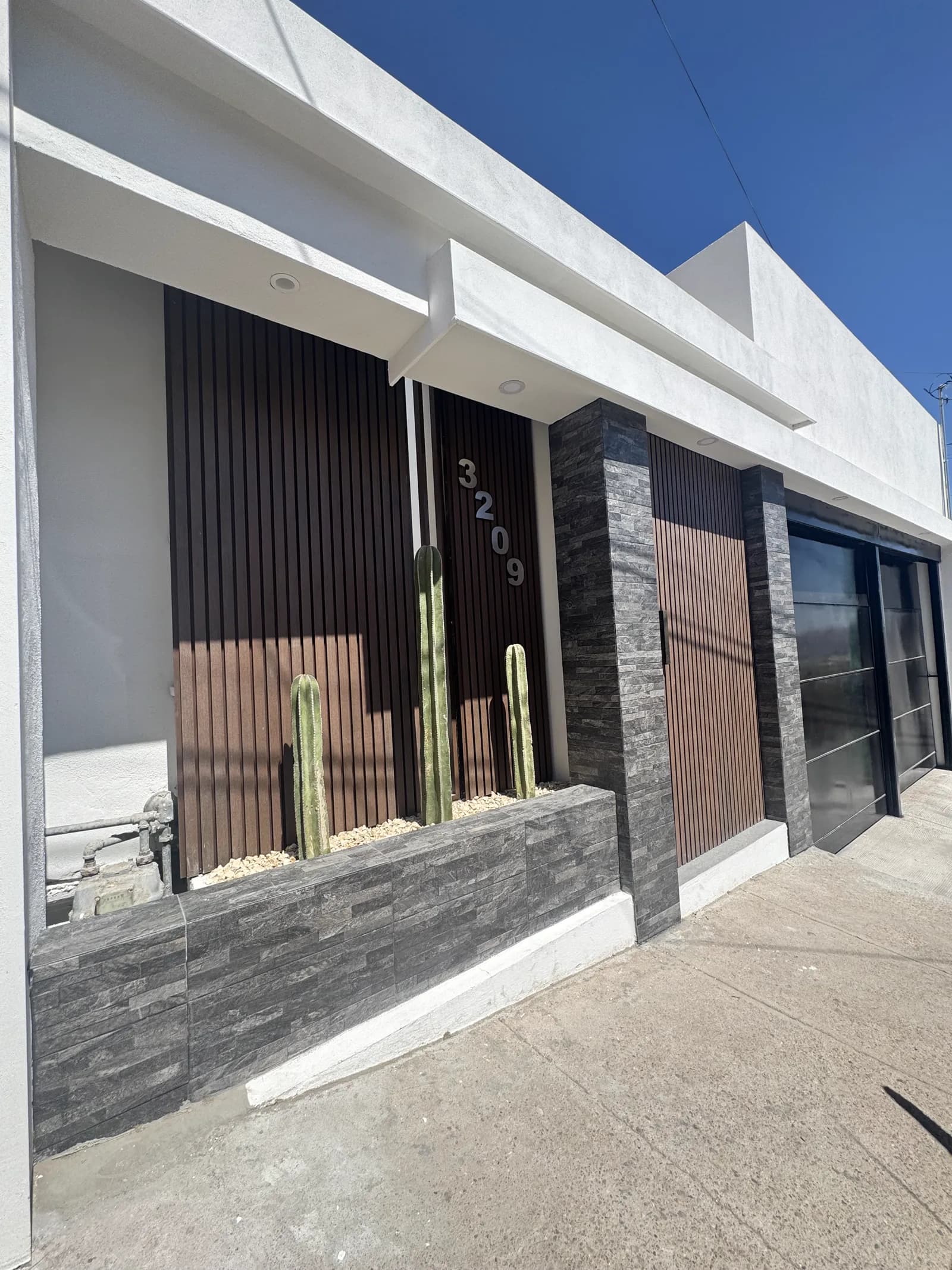 Fachada terminada en perspectiva, con los listones de madera, la piedra laja y el portón negro.