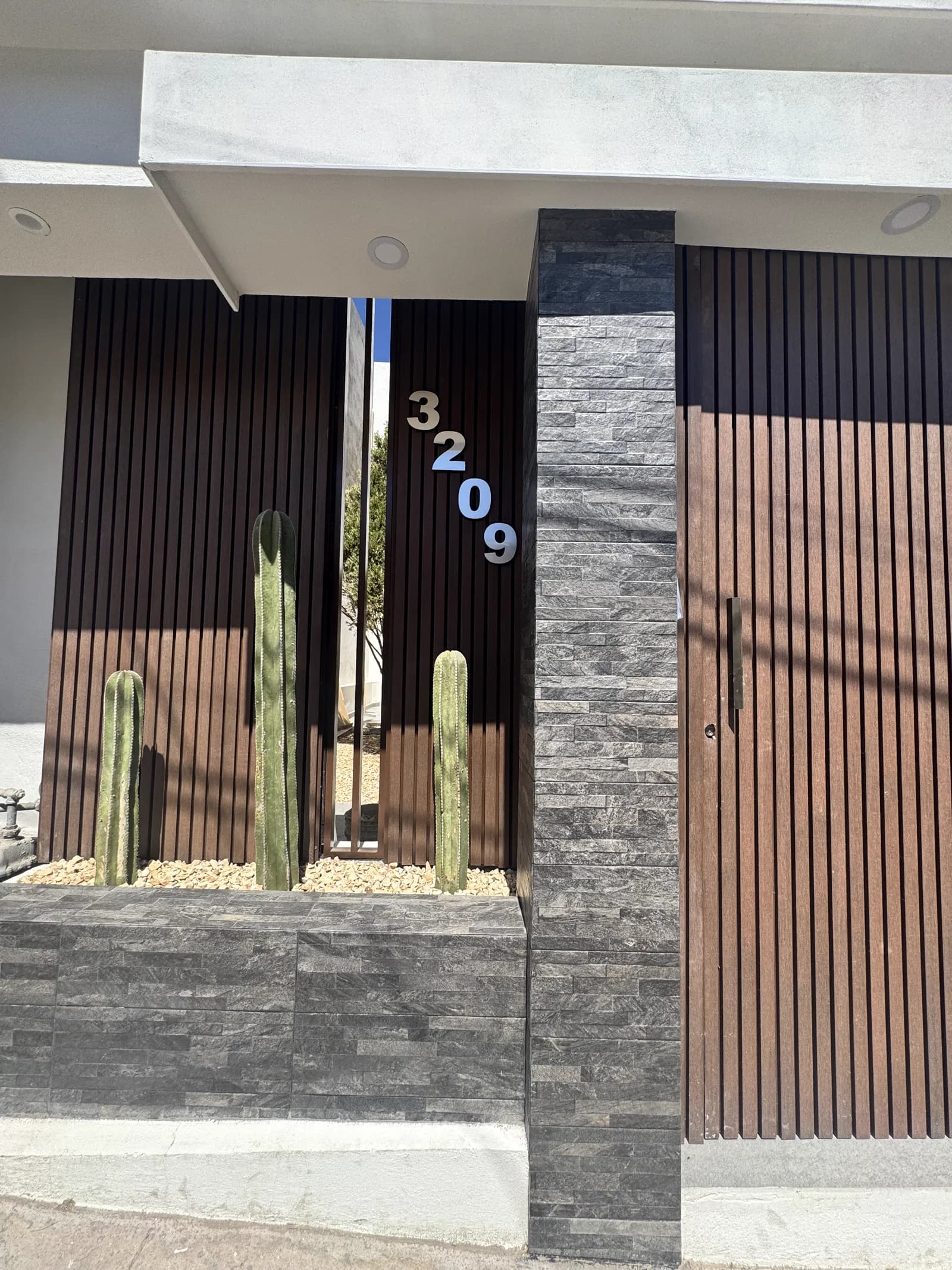 Acceso de Casa Barrancas 02, con listones de madera, columna de piedra laja gris y una jardinera de cactáceas.