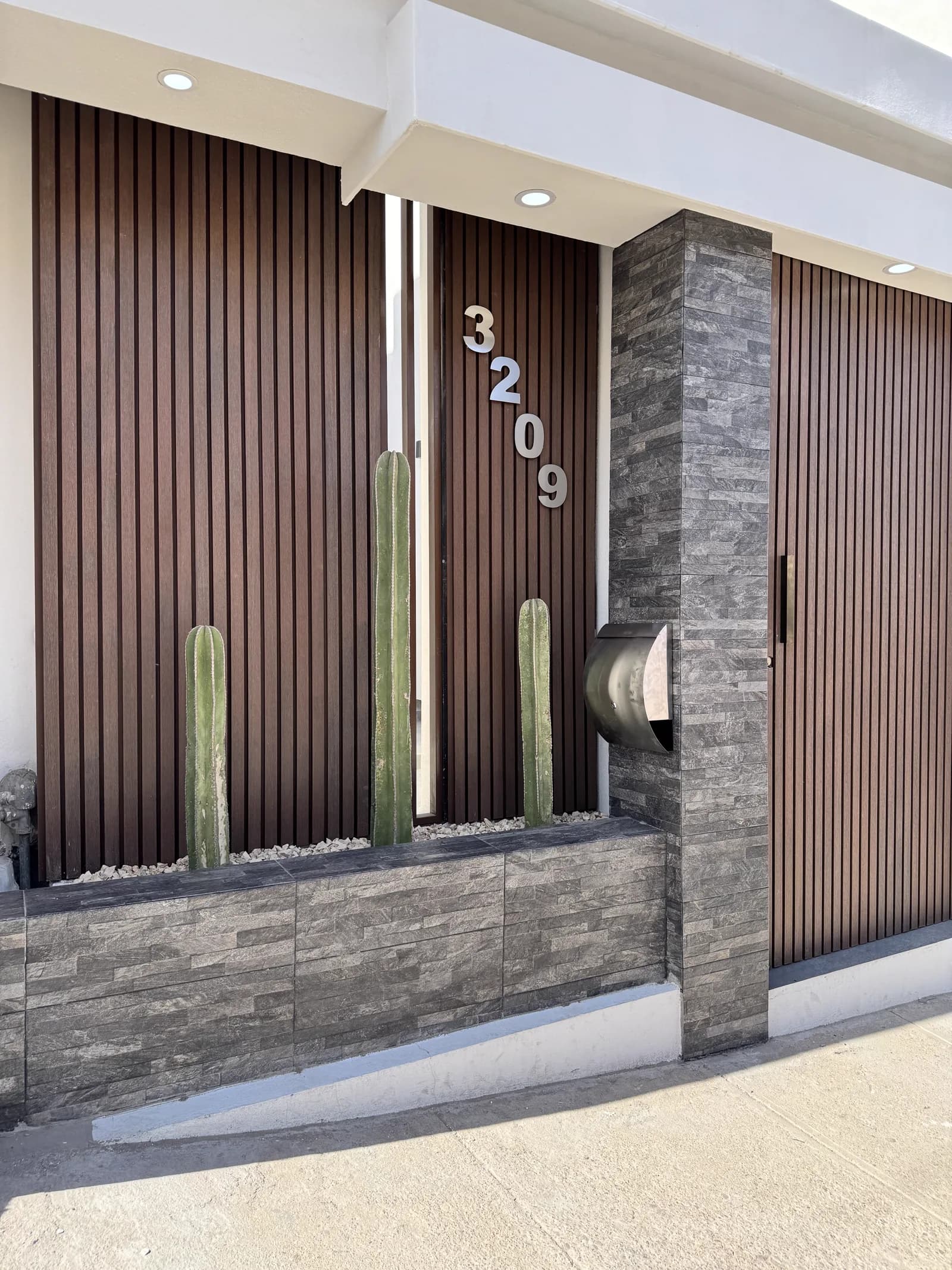 Acceso con la jardinera de piedra, el buzón metálico y los listones de madera.