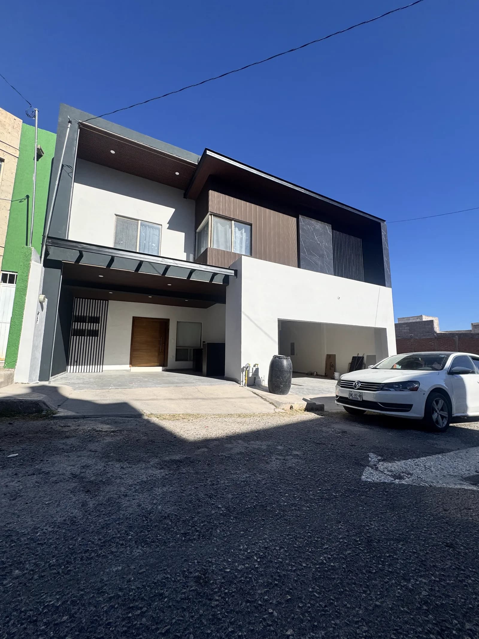 Fachada terminada de Casa Barrancas 03, con aplanado blanco, volumen de madera y marco negro.