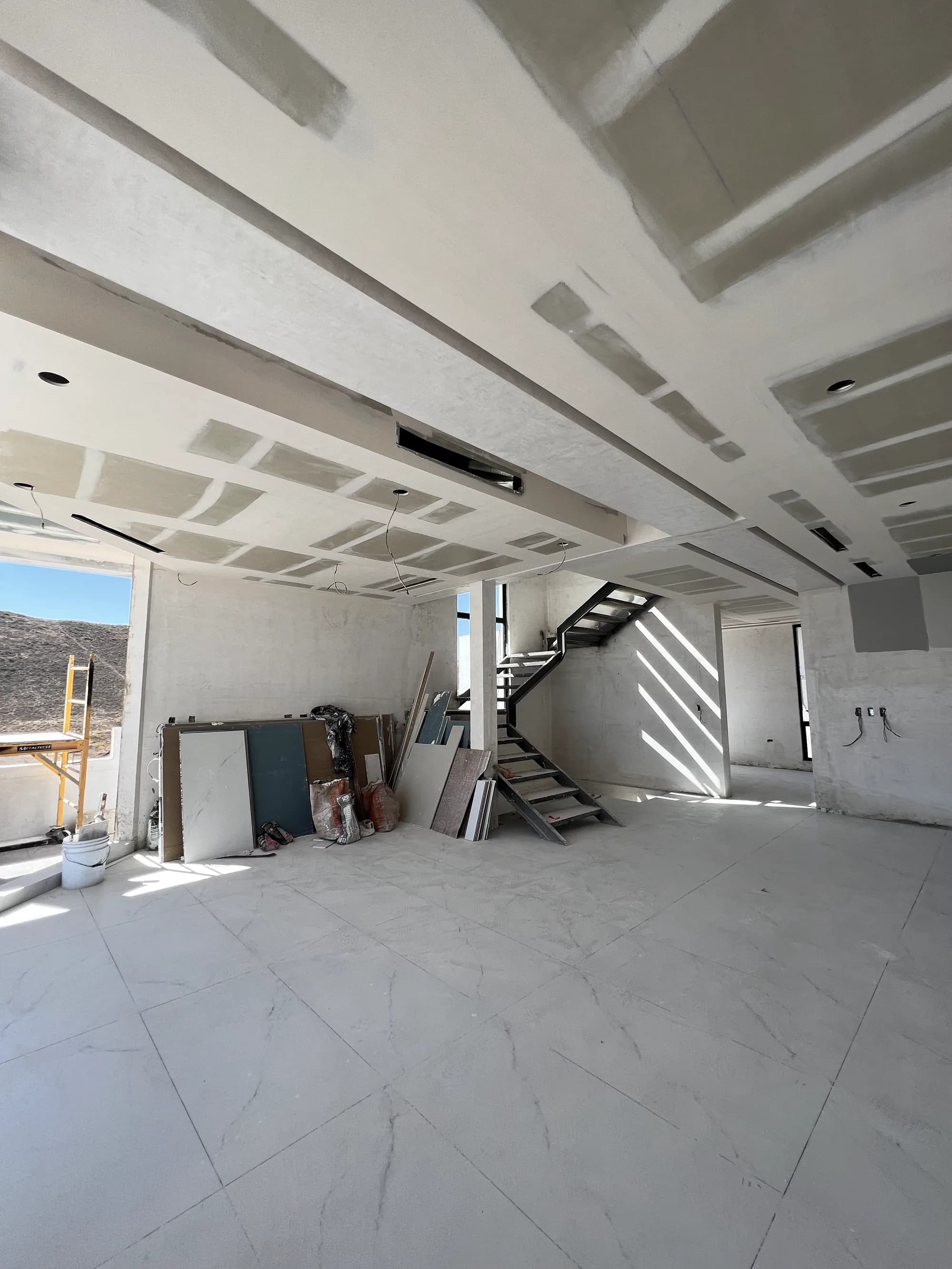 Interior en obra con los plafones ya trazados, el piso puesto y la escalera.