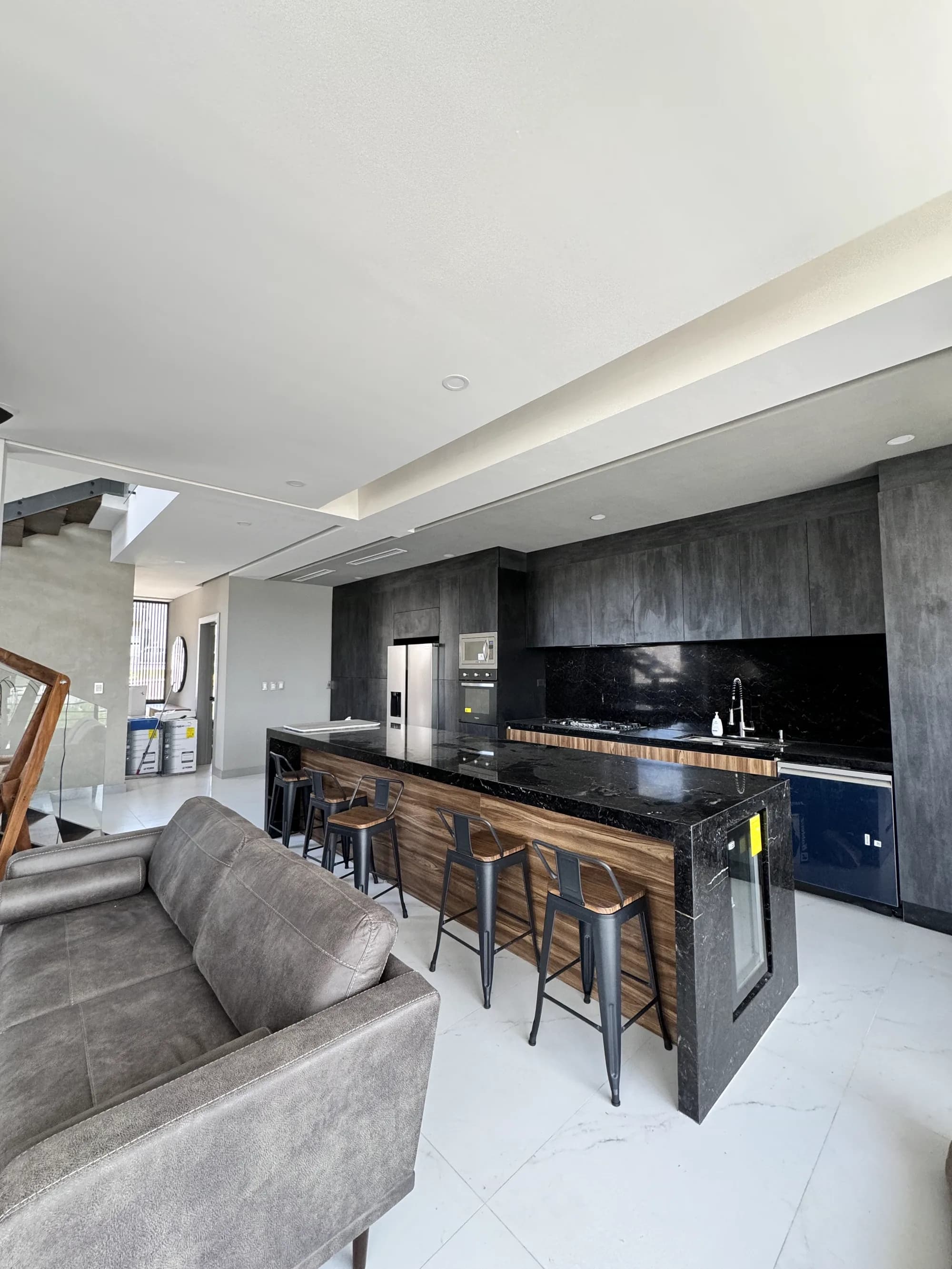Sala y cocina terminadas, con la isla de mármol negro y madera y los bancos altos.