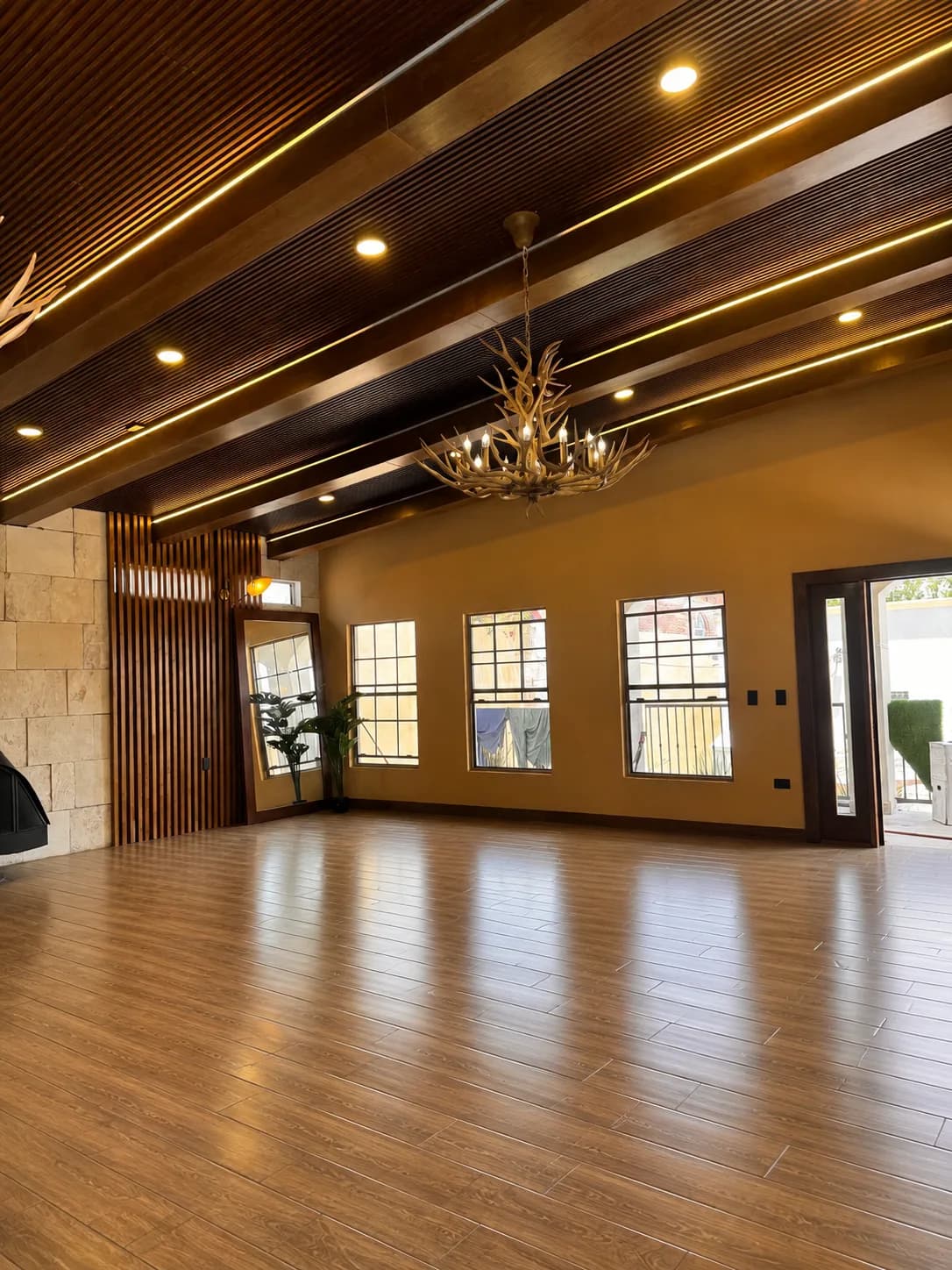 Salón de Casa Casas Grandes, con piso de madera, plafón de duela oscura con vigas y un candil de astas.