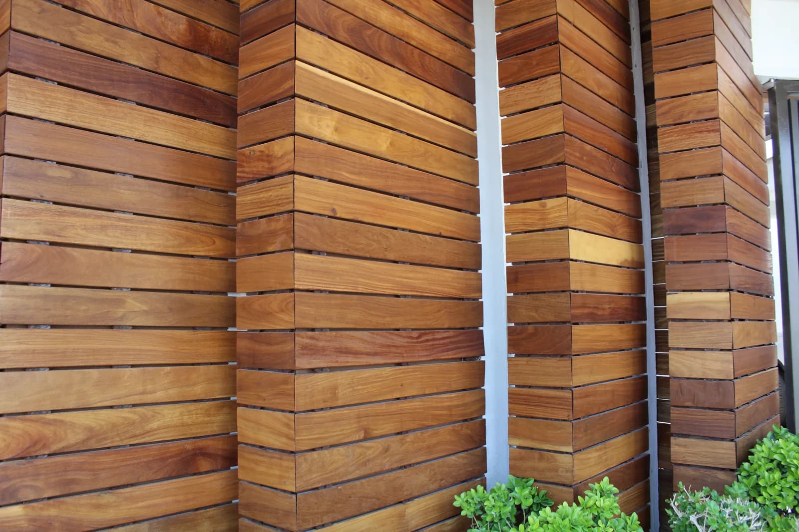 Detalle del muro de listones de madera natural con vegetación al pie.