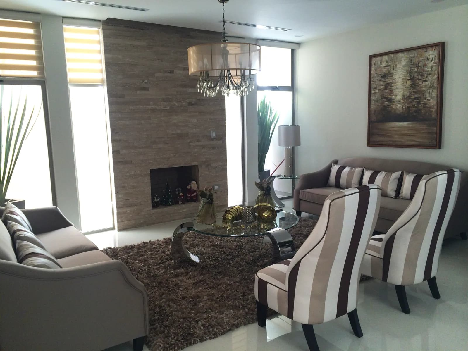 Sala con chimenea revestida de piedra, sillones de rayas y candil.