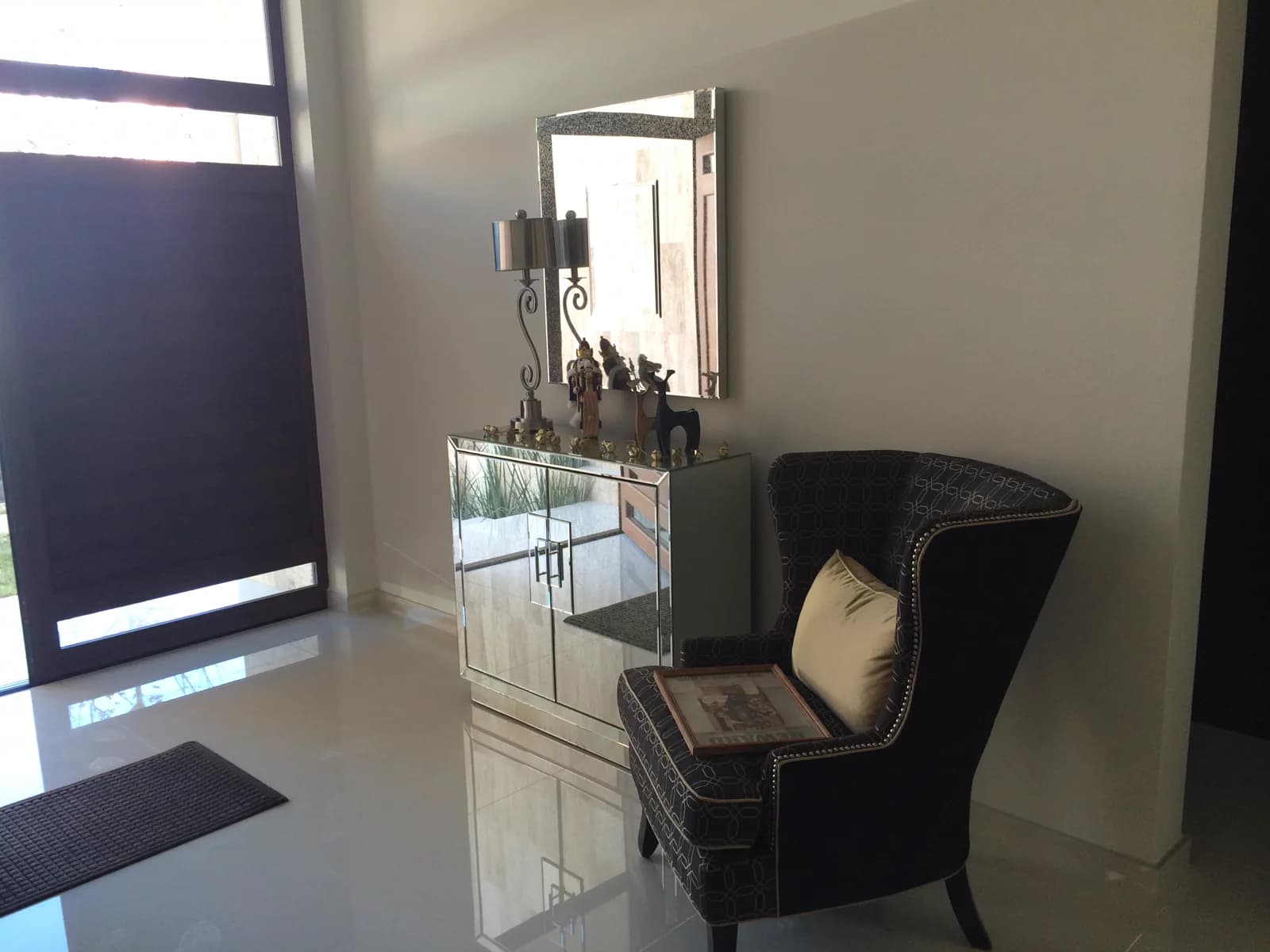 Recibidor con consola de espejo y sillón de respaldo alto junto a la puerta.
