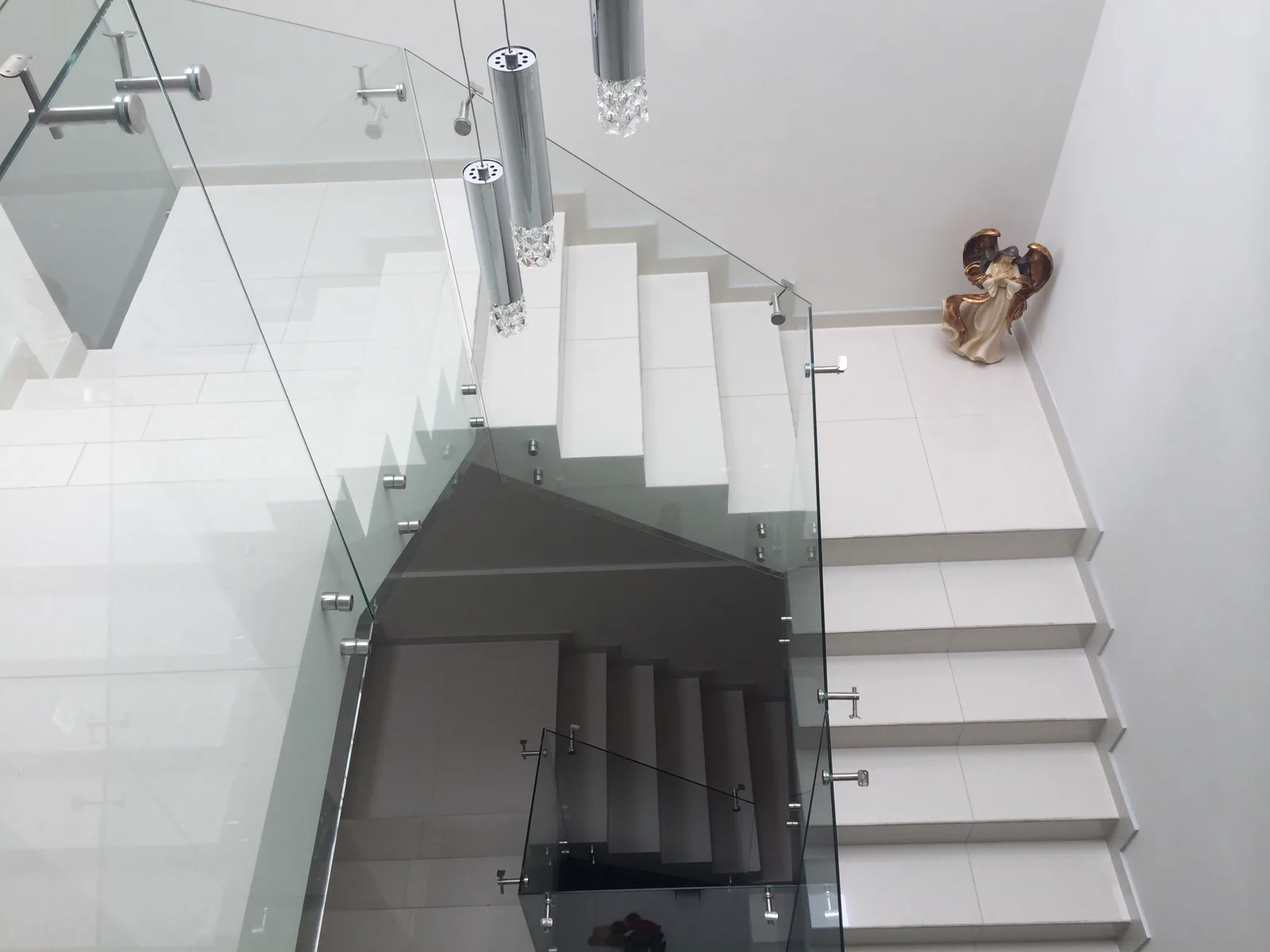 Escalera de peldaños blancos con barandal de cristal, vista desde arriba.