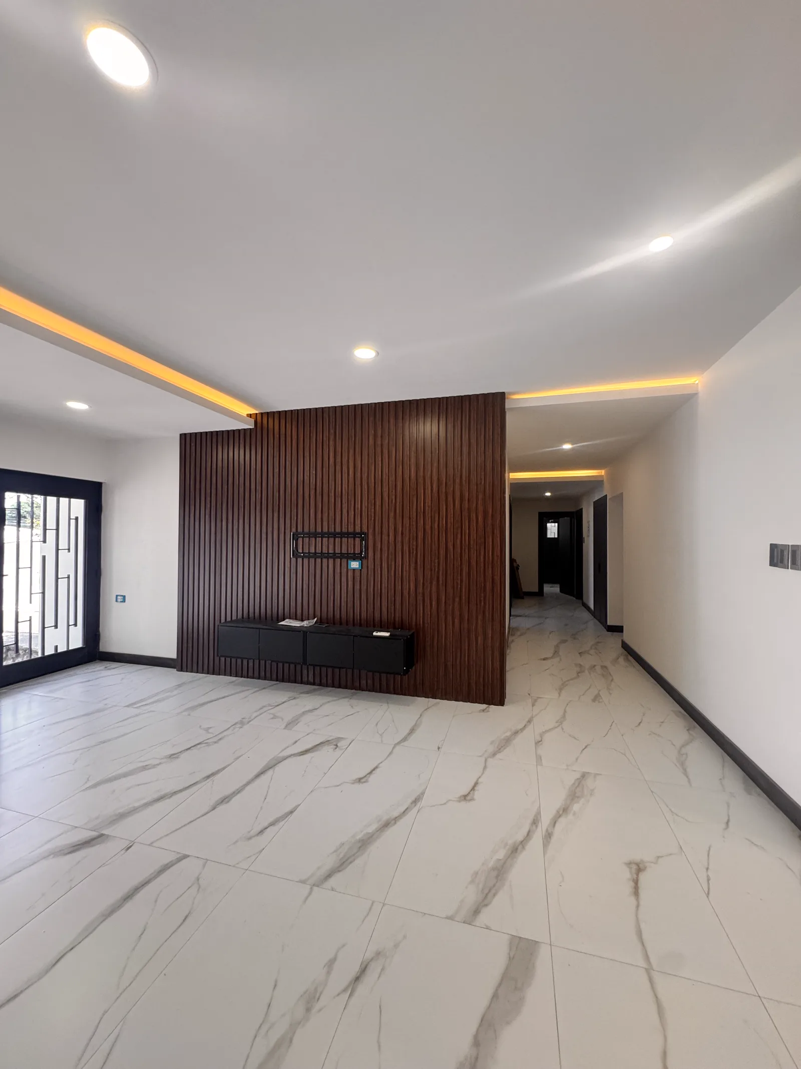 Estancia terminada con el muro de madera oscura y el plafón con luz indirecta.
