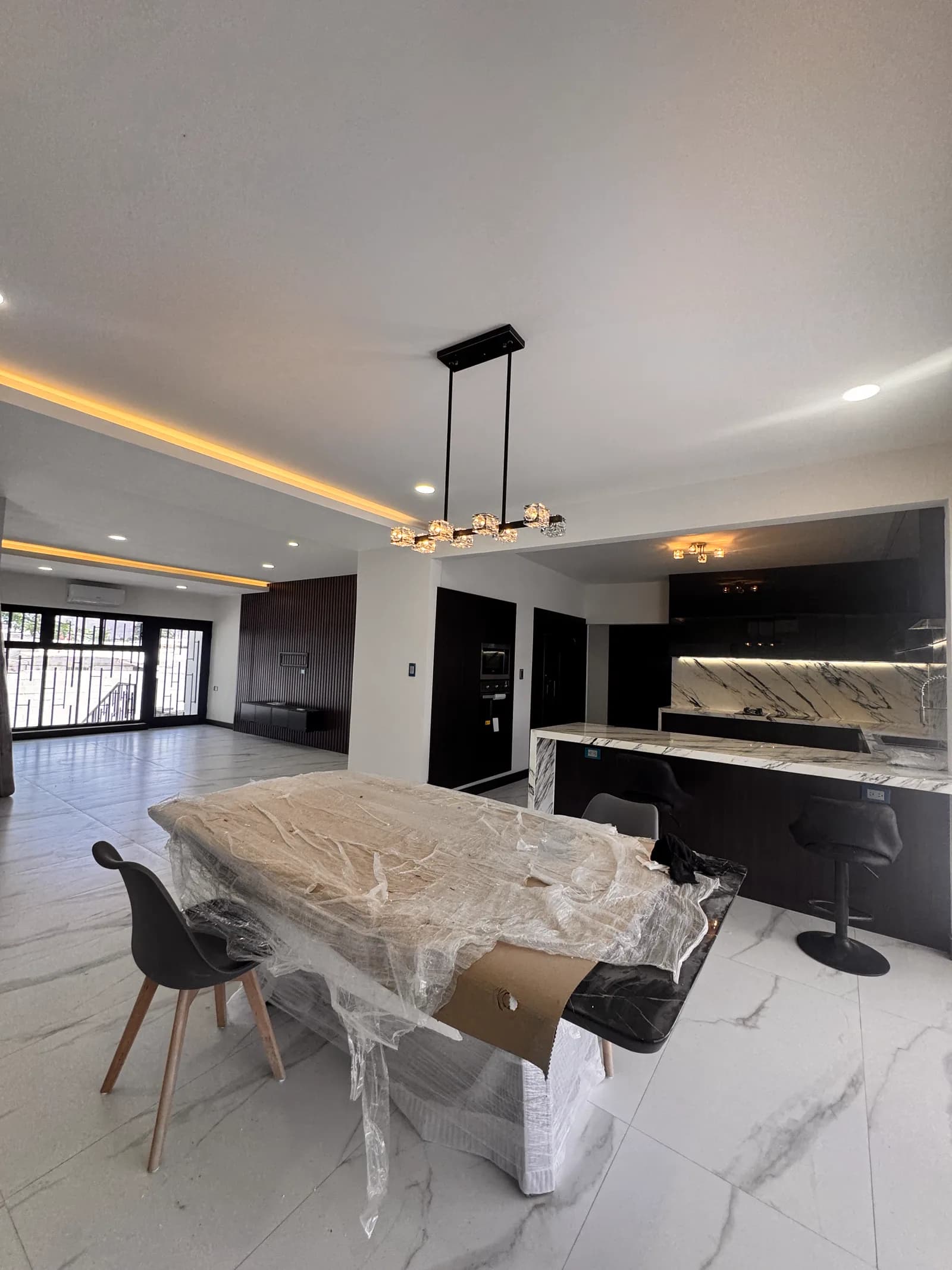 Comedor con lámpara lineal y la cocina de gabinetes negros al fondo.