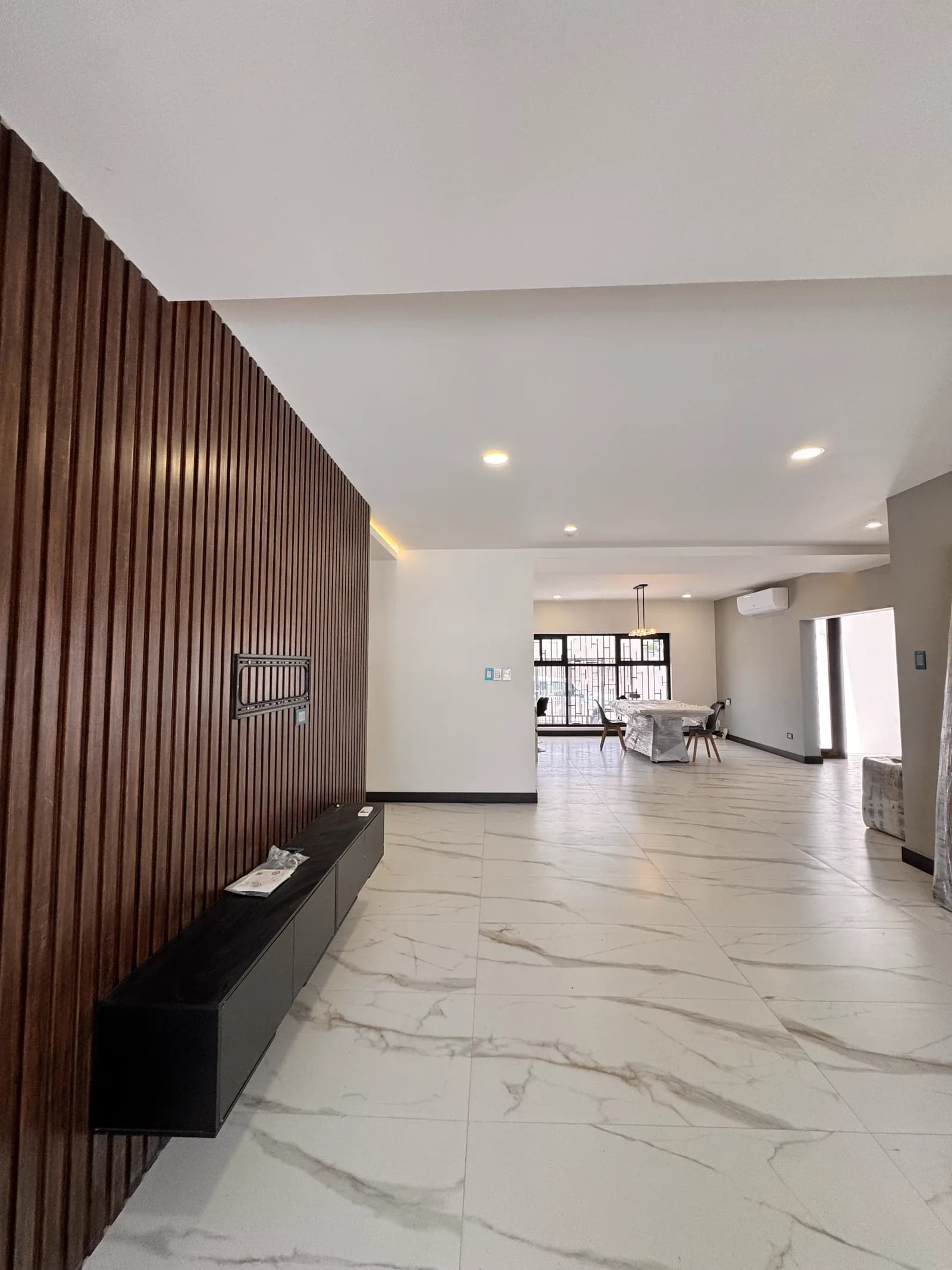 Muro de listones de madera oscura con mueble flotante y el comedor al fondo.