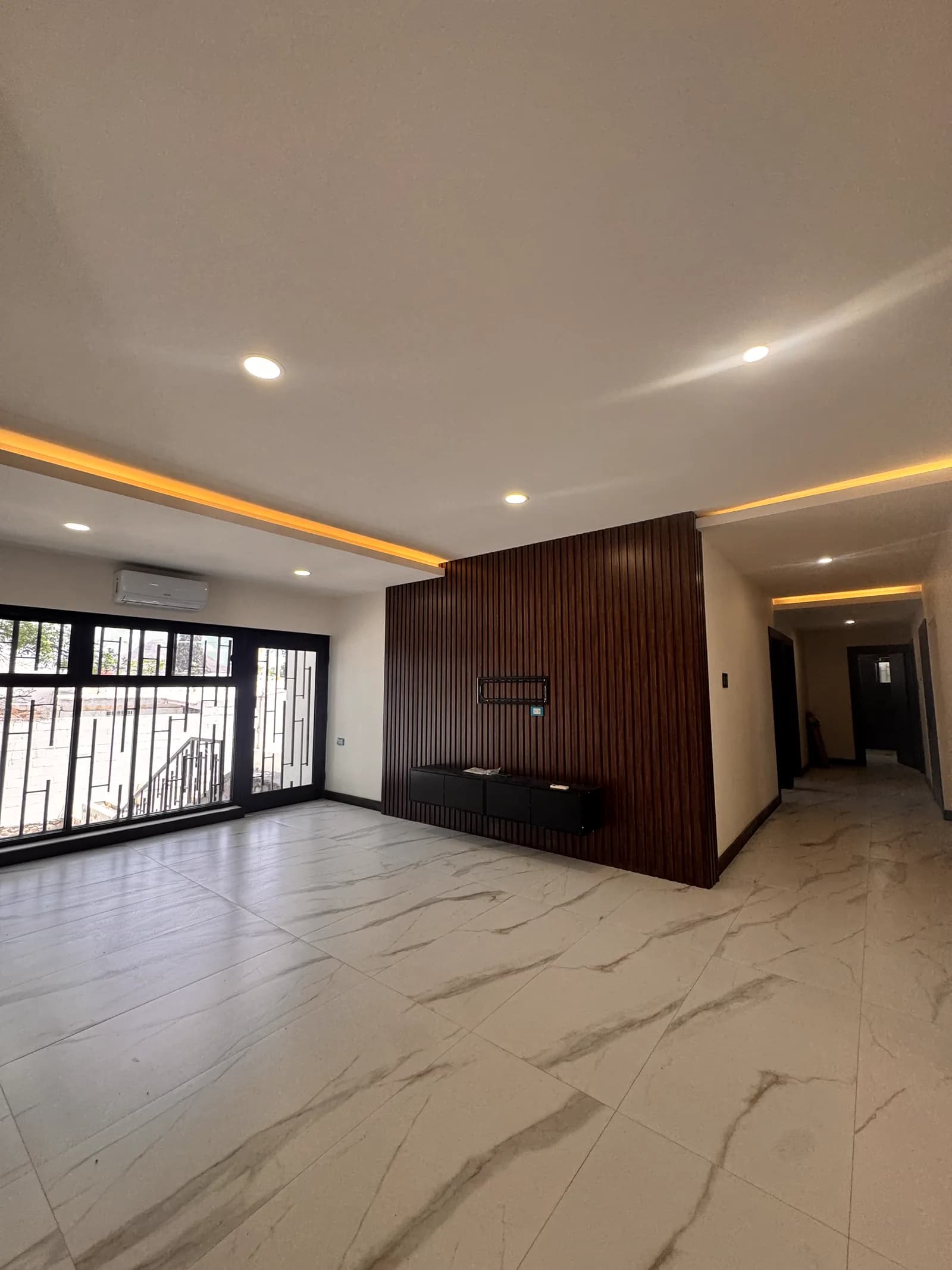 Estancia terminada de Casa Mirador, con piso de porcelanato veteado, plafón con luz indirecta y muro de madera oscura.
