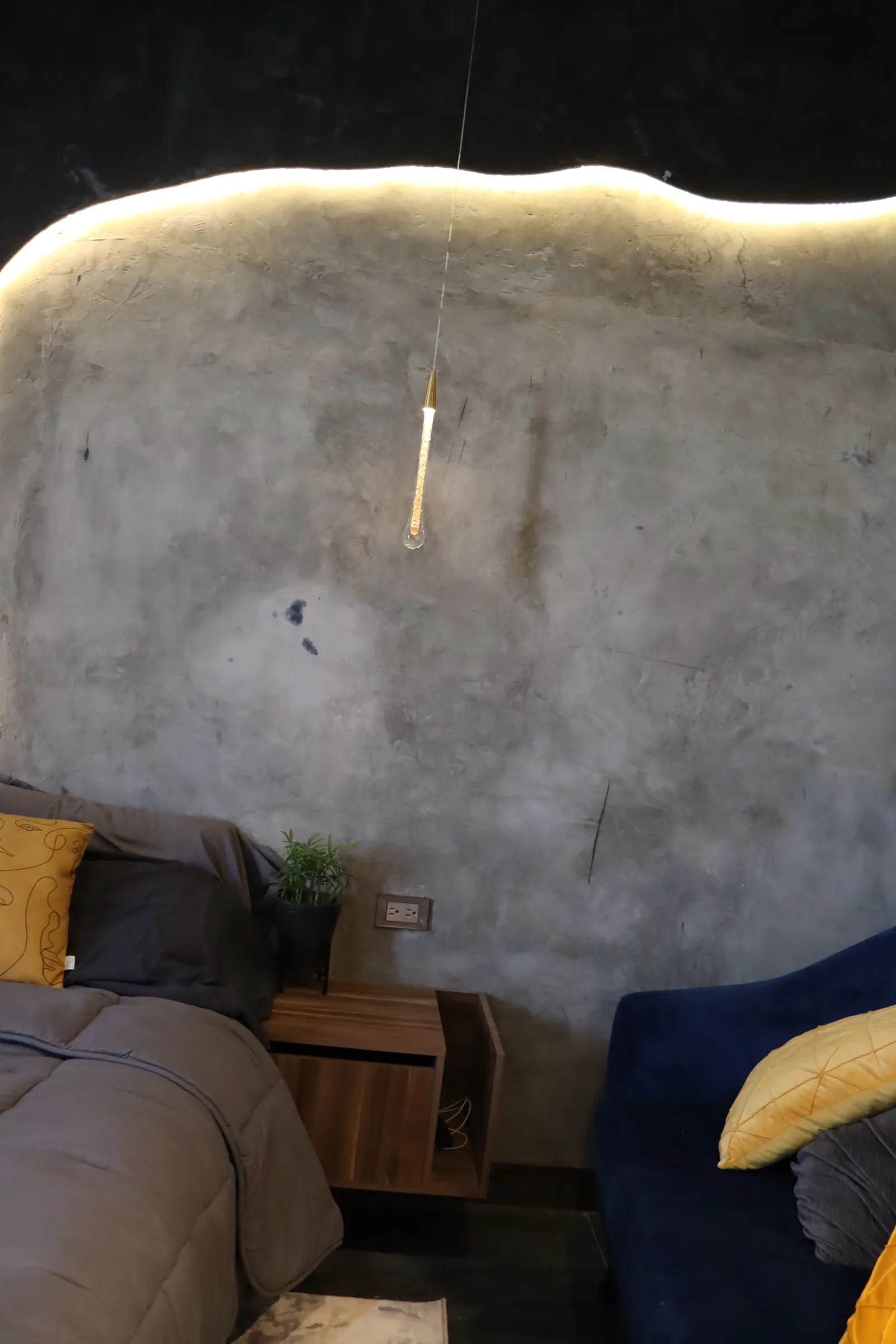 Cabecera de concreto pulido con luz en el borde curvo y una lámpara de gota suspendida.
