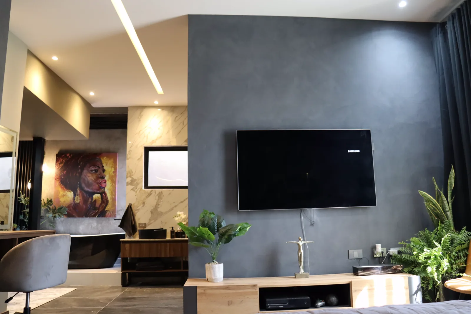 Recámara hacia el baño abierto, con muro gris, pantalla y mueble de madera.