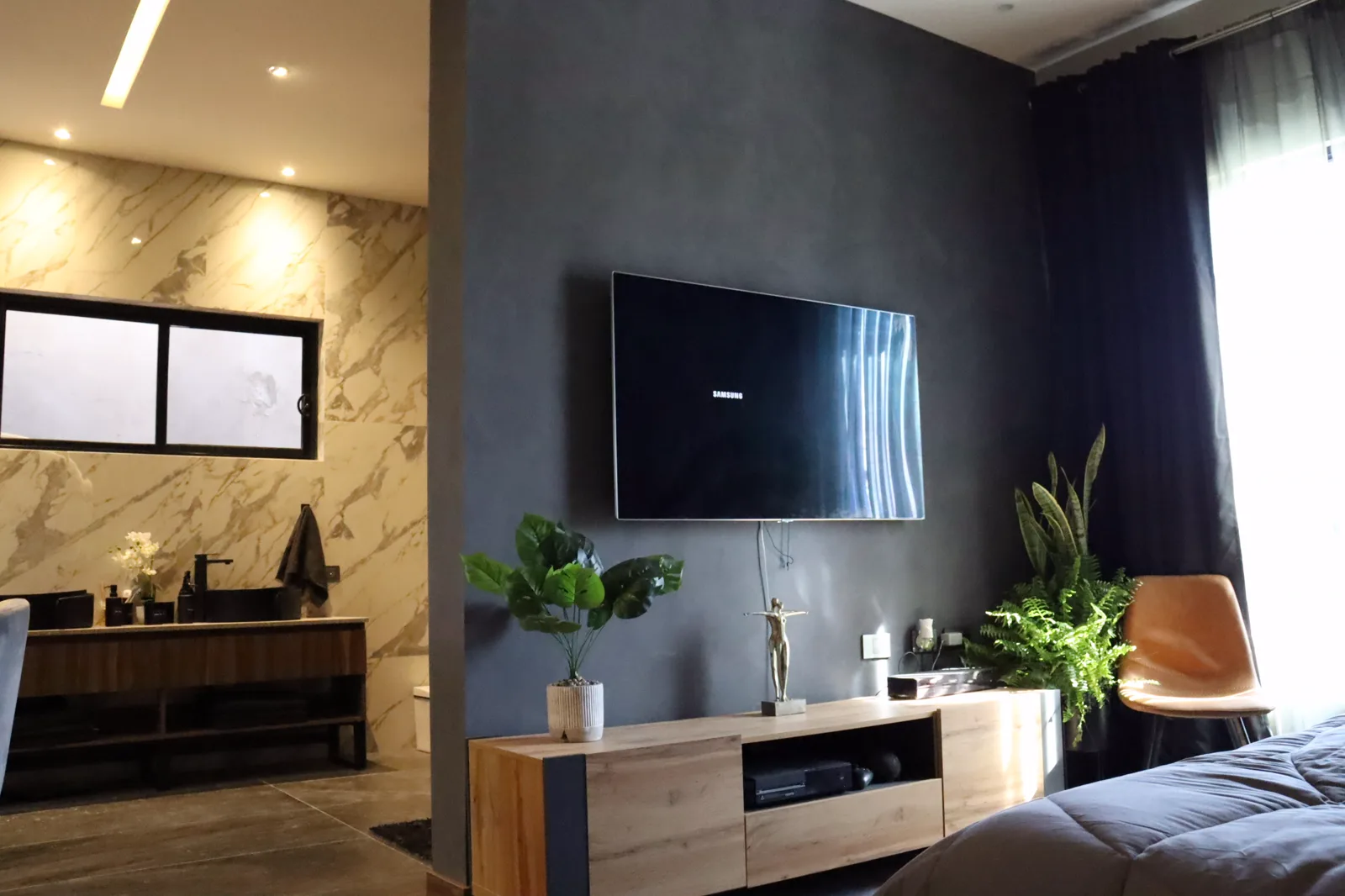 Muro gris con la pantalla y el mueble de madera, con el baño de mármol detrás.