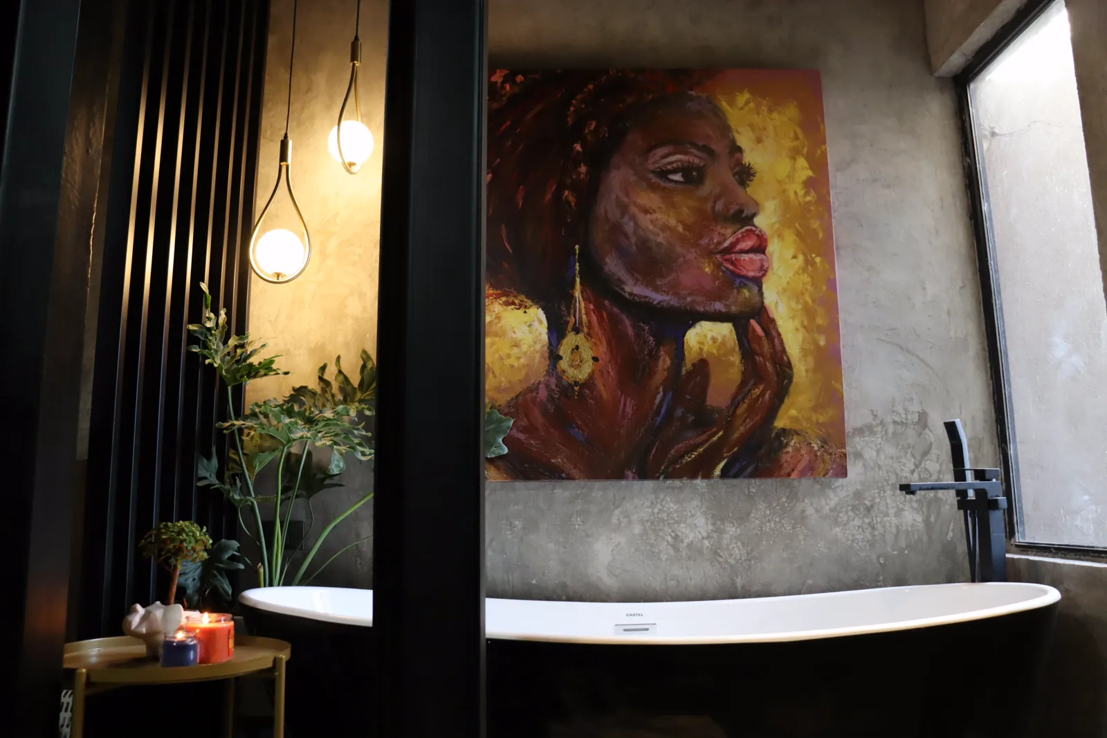Baño de Casa P-T, con tina exenta negra, muro de concreto pulido, lámparas de globo y un cuadro de gran formato.