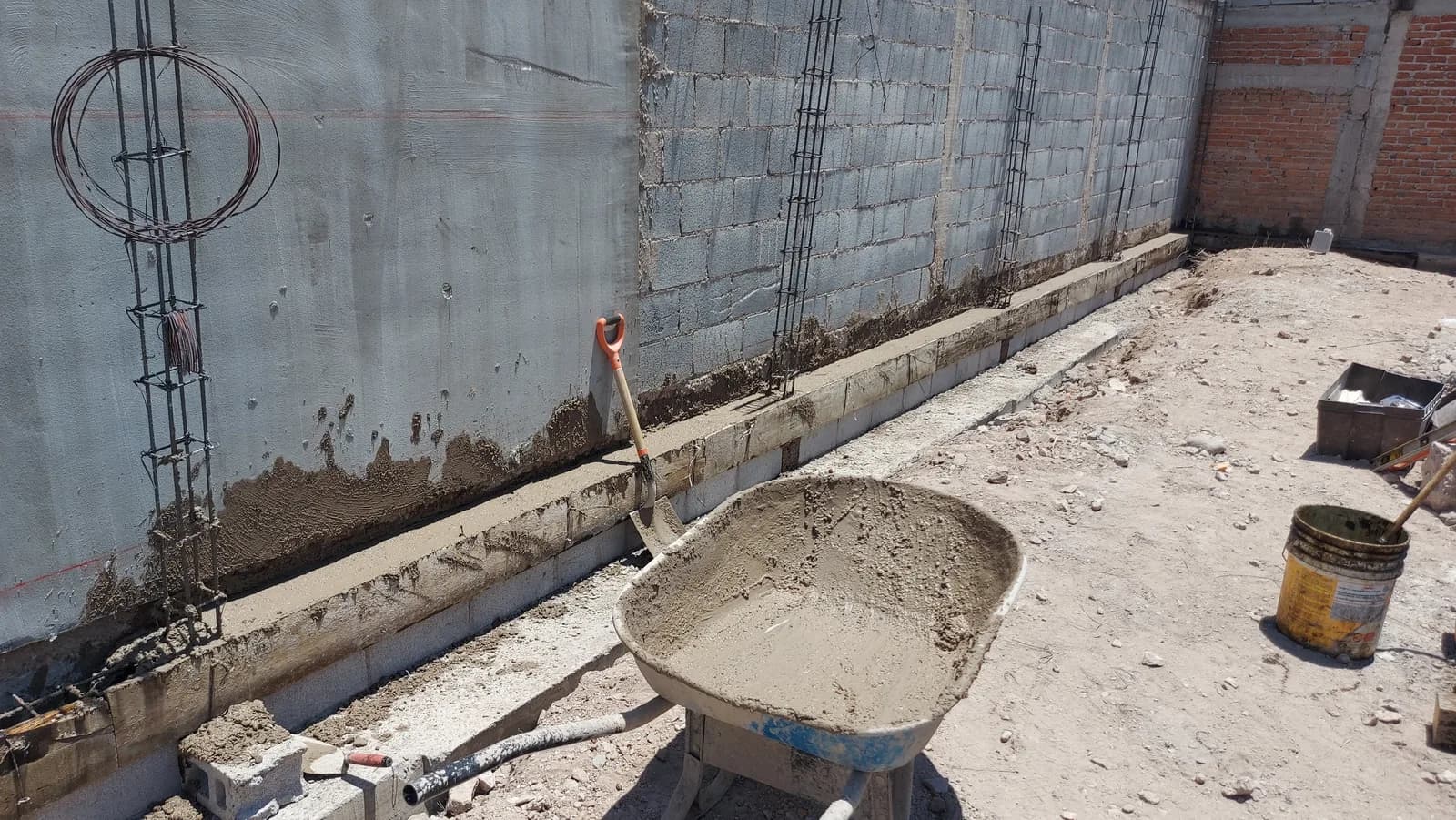 Cadena de cimentación colada contra el muro de contención, con el armado de acero saliendo de los castillos.