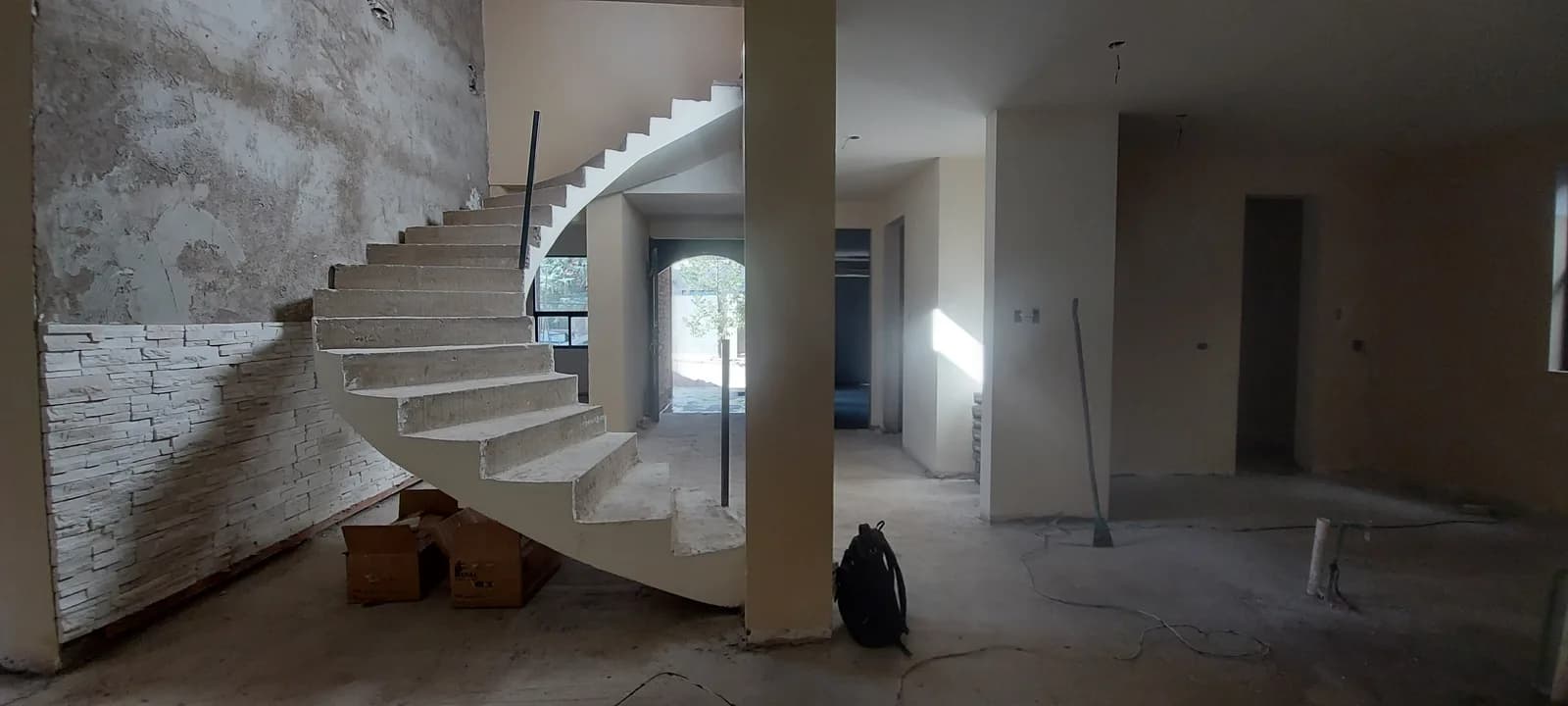 Escalera helicoidal terminada en concreto, junto al muro de piedra de la planta baja.