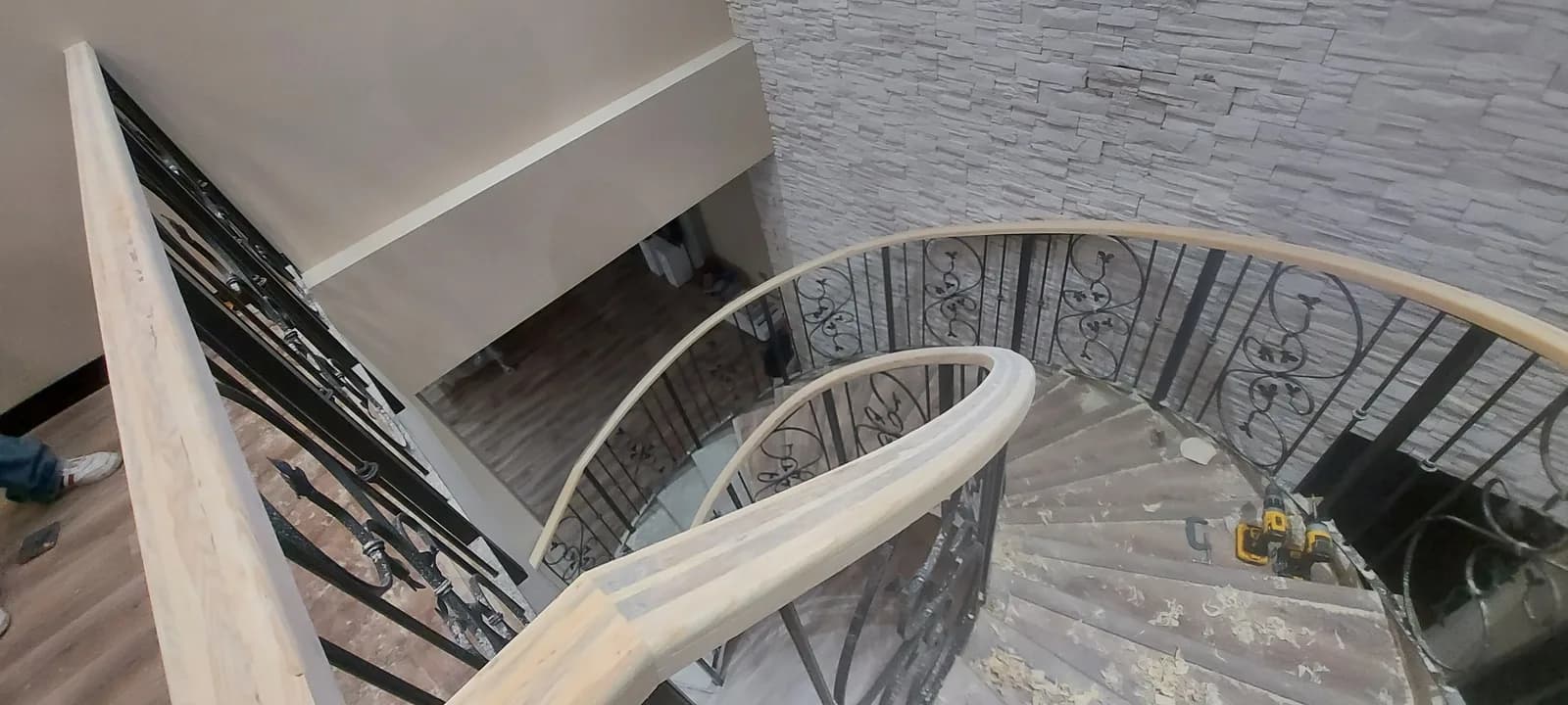 Escalera vista desde el descanso alto, con el barandal de herrería negra y el pasamanos de madera.