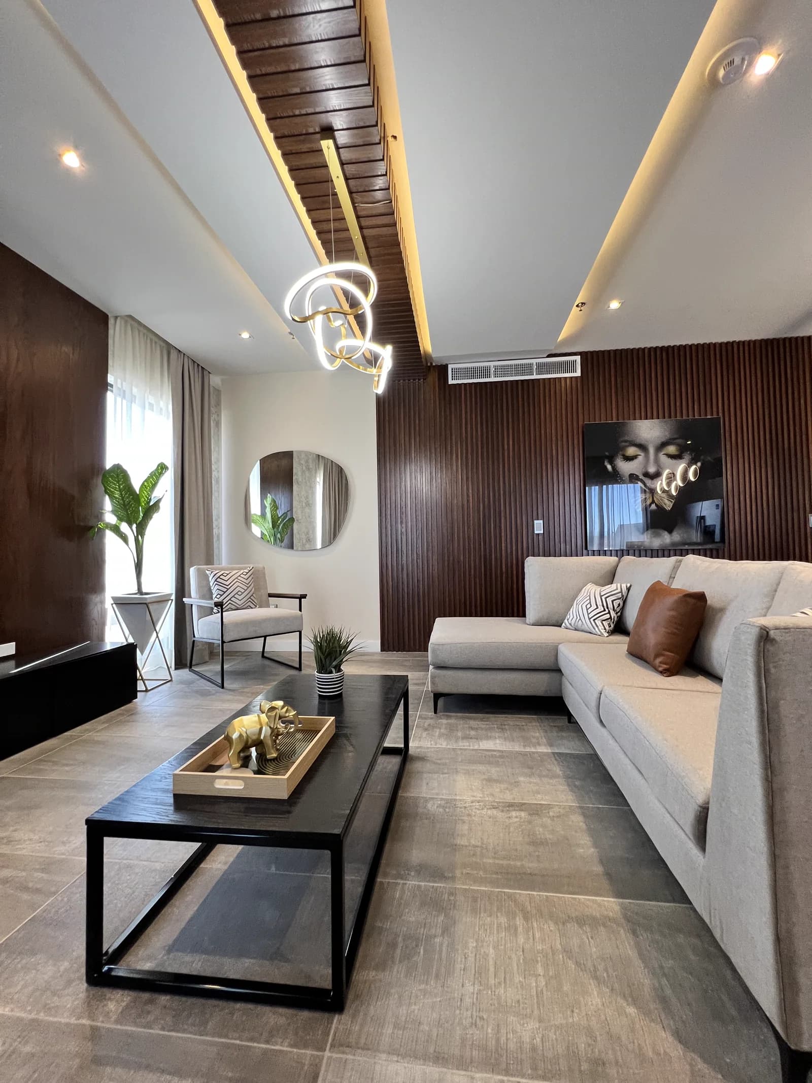 Sala con mesa de centro negra y muro de listones de madera bajo el plafón iluminado.