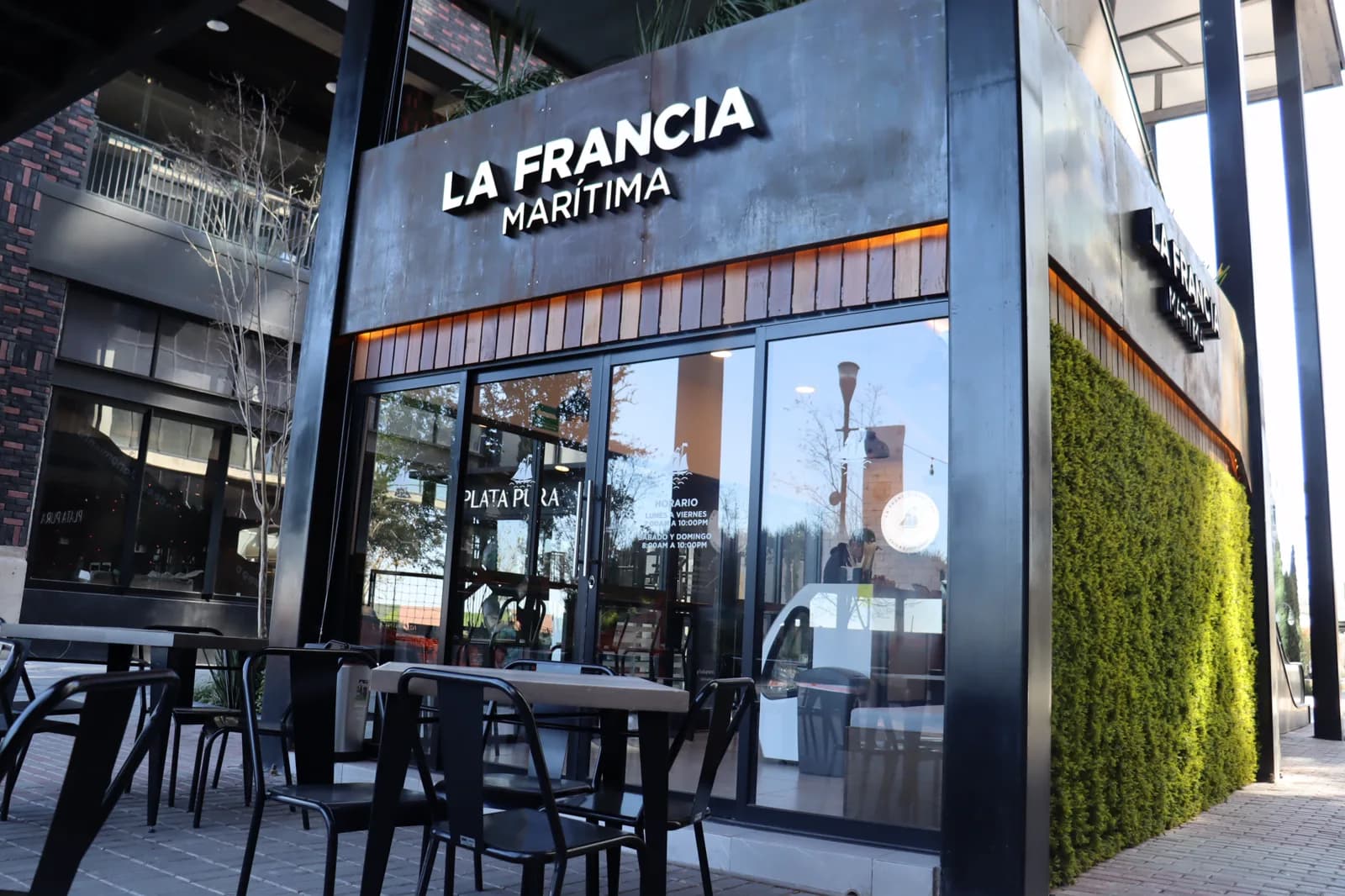 Acceso de La Francia Marítima, con el muro verde y la terraza con mesas.