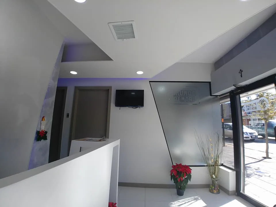Recepción de Mundo Dental Centro, con mostrador blanco, muros en diagonal y luz azul indirecta.
