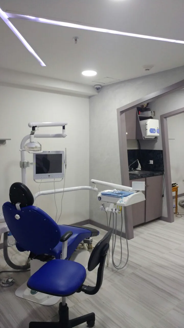 Consultorio con sillón dental azul y piso tipo madera gris.
