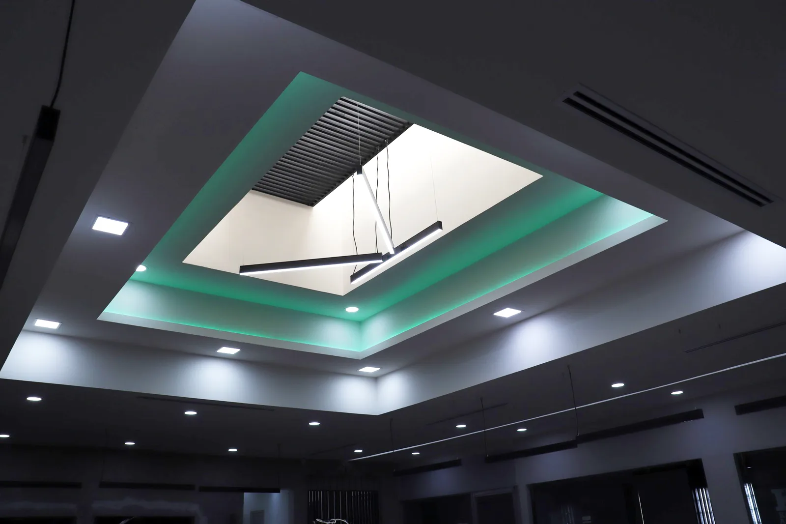 Tragaluz enmarcado por el plafón con luz verde indirecta y lámparas lineales.