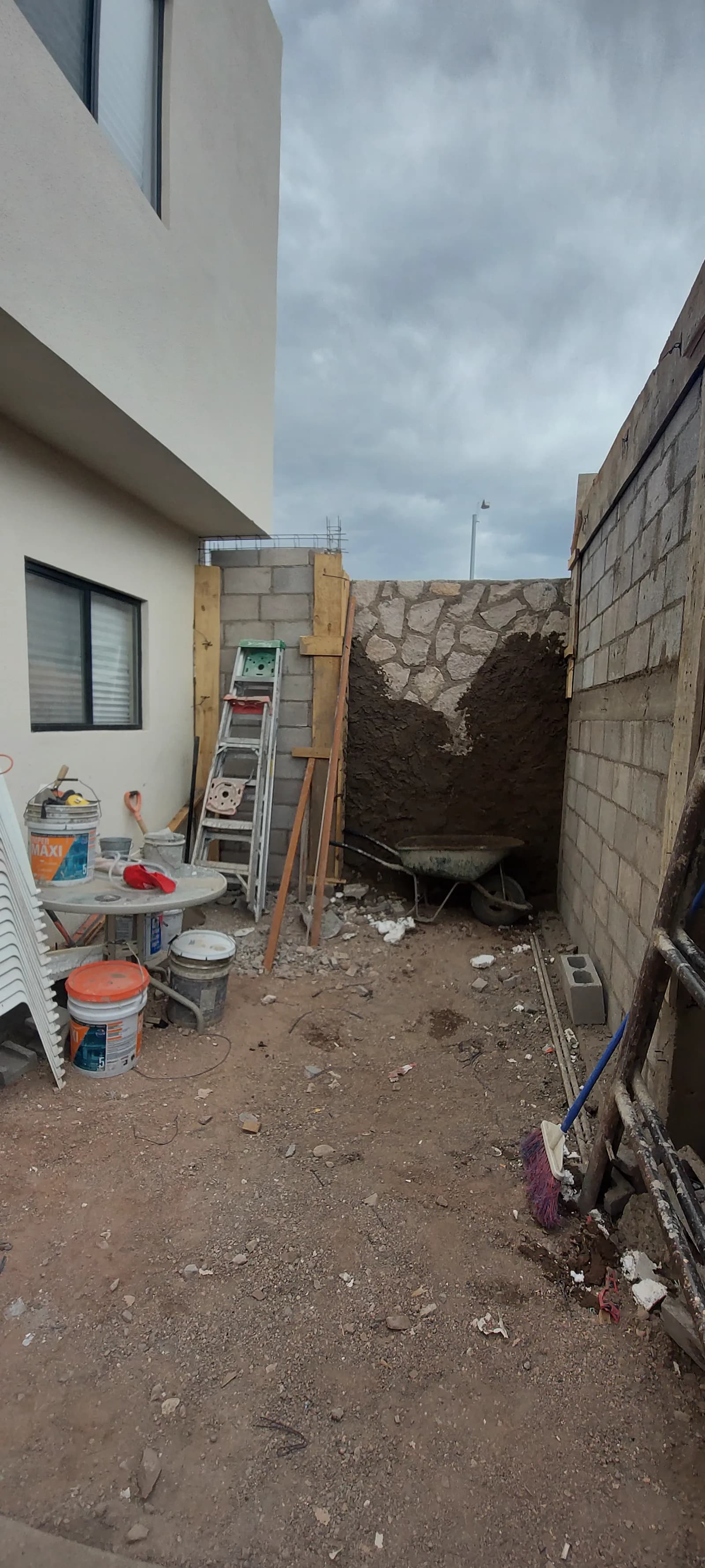 El patio antes de la obra, con piso de tierra y material de construcción.