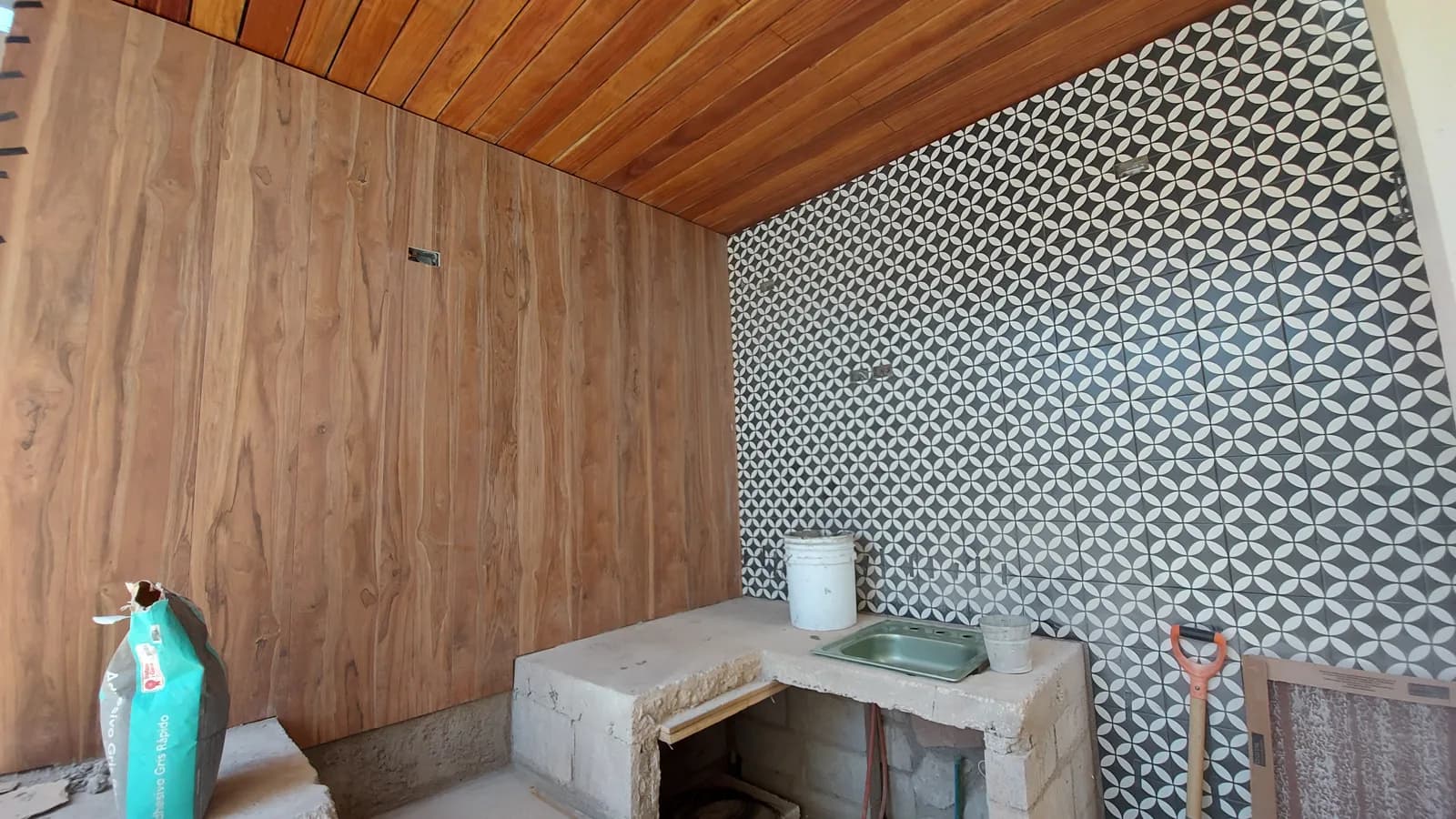 La barra en obra frente al muro de madera y el mosaico.