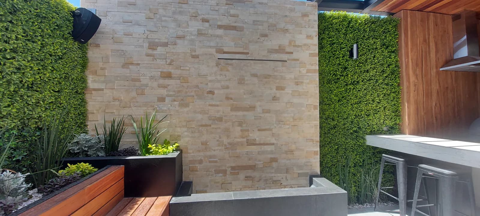 Jardinera de madera y muros verdes junto al muro de piedra laja clara.