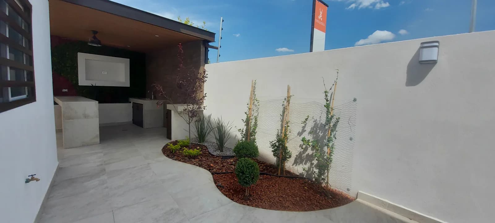 Jardín con árboles jóvenes y corteza roja junto al muro blanco.