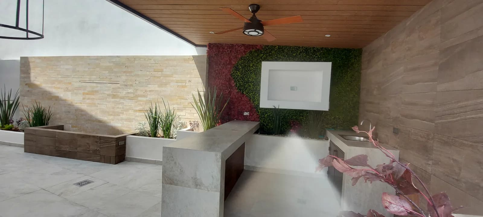 Terraza con la pantalla enmarcada en el muro verde y la barra.
