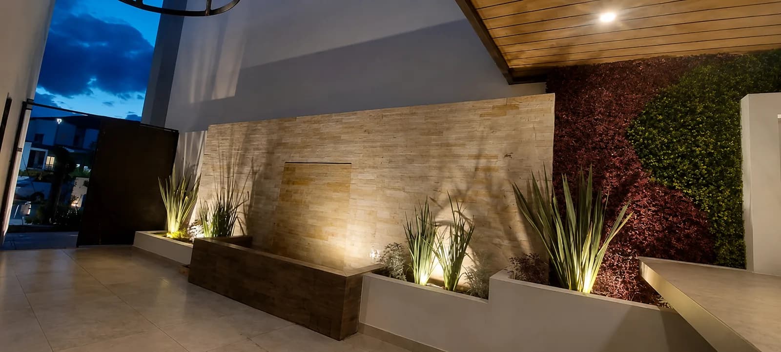 El patio al anochecer, con las jardineras y la caída de agua iluminadas.