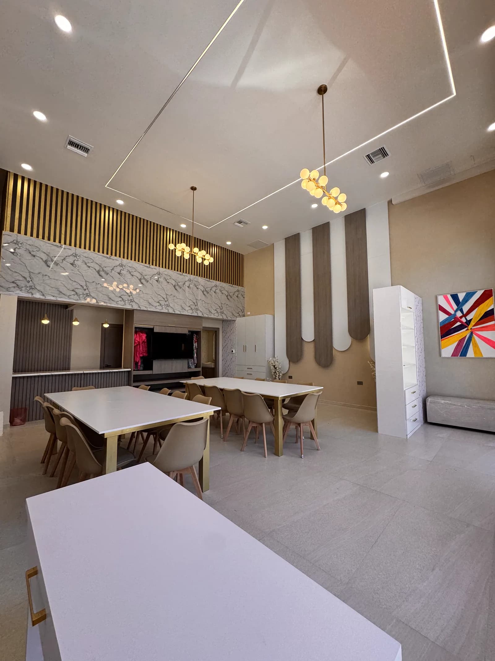 Salón con mesas largas, columnas de listones en arco y un cuadro de colores.