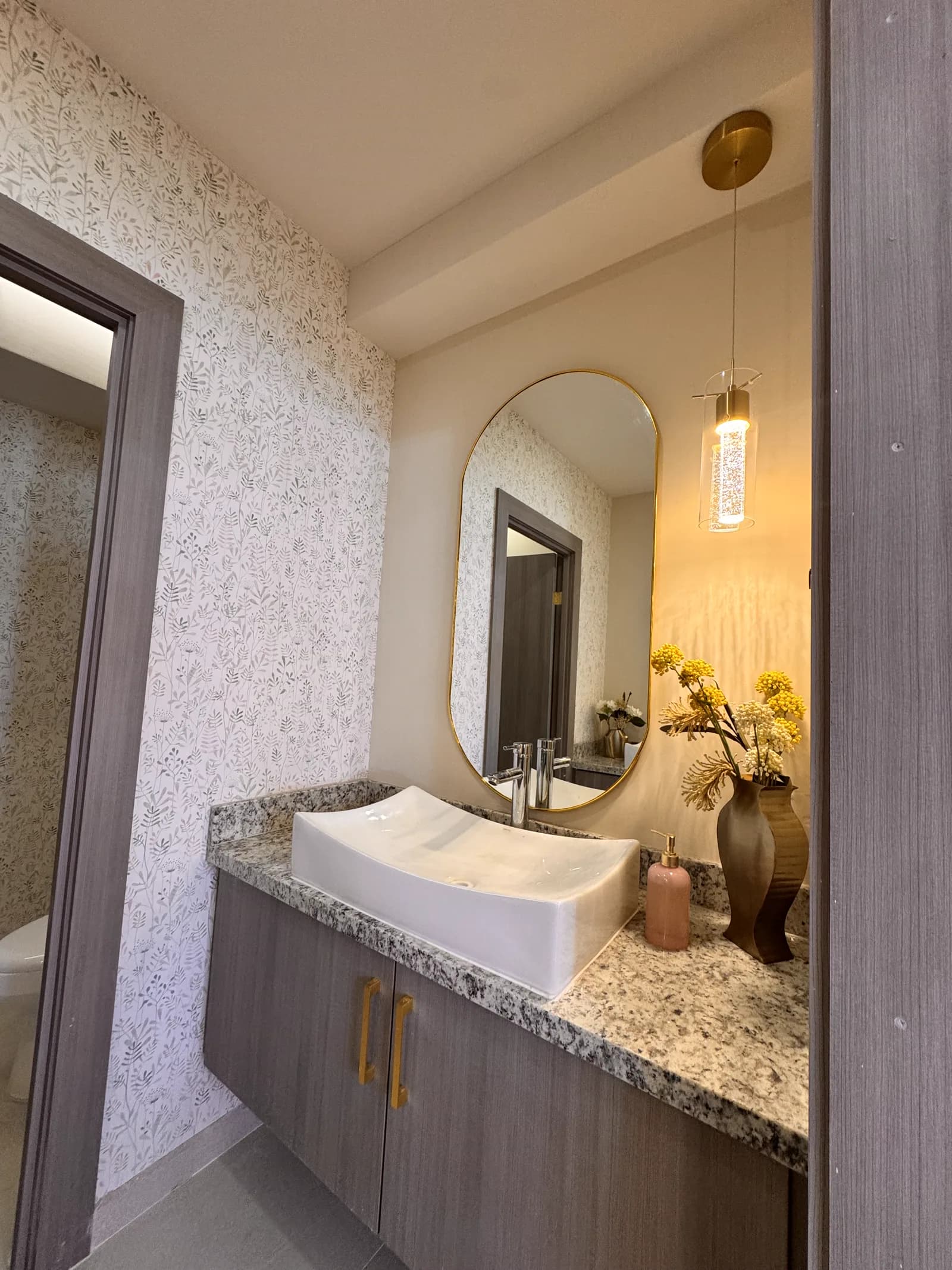 Tocador con lavabo blanco, espejo ovalado y papel tapiz floral.
