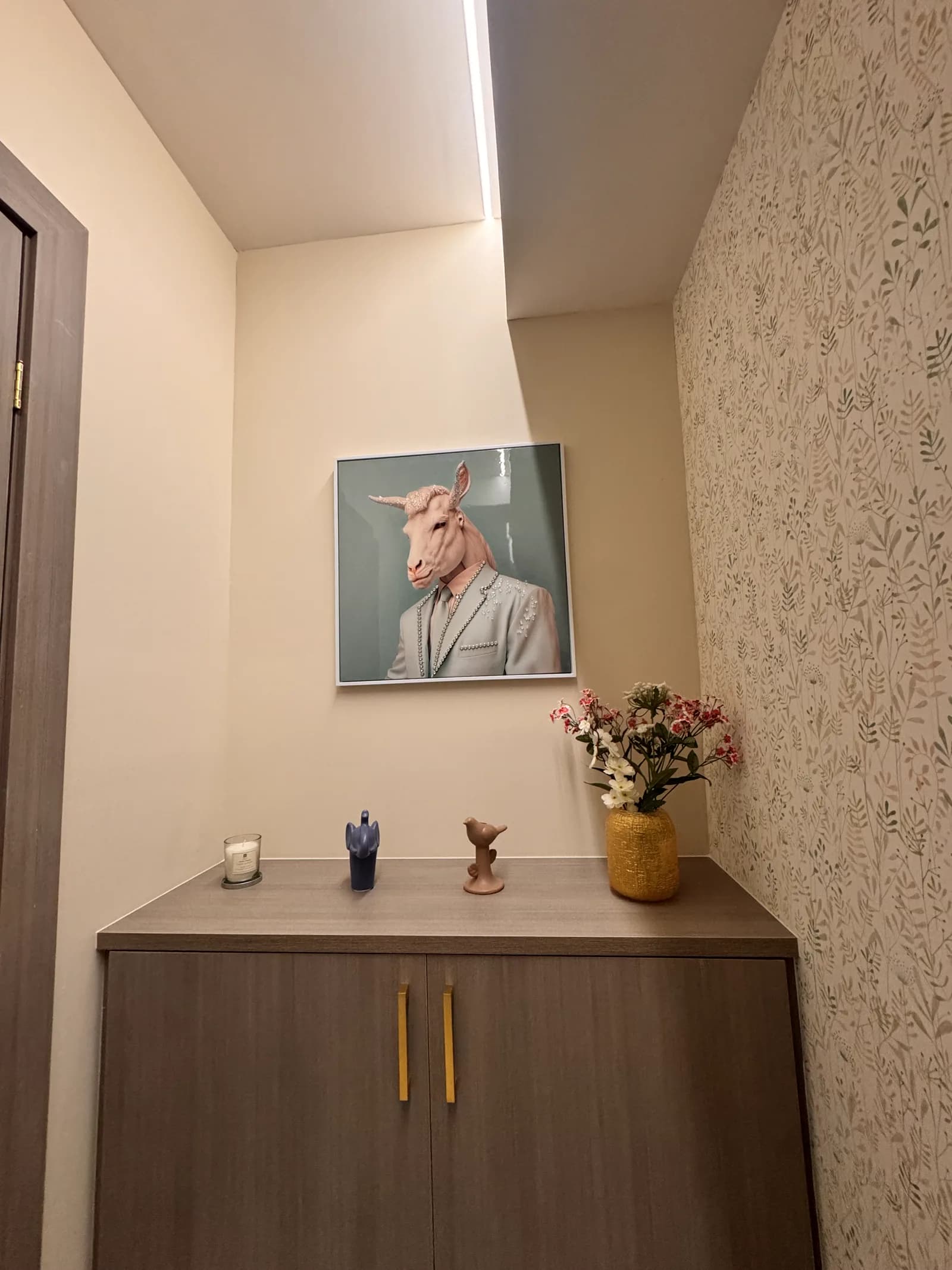 Mueble de madera con cuadro y flores frente al papel tapiz floral.