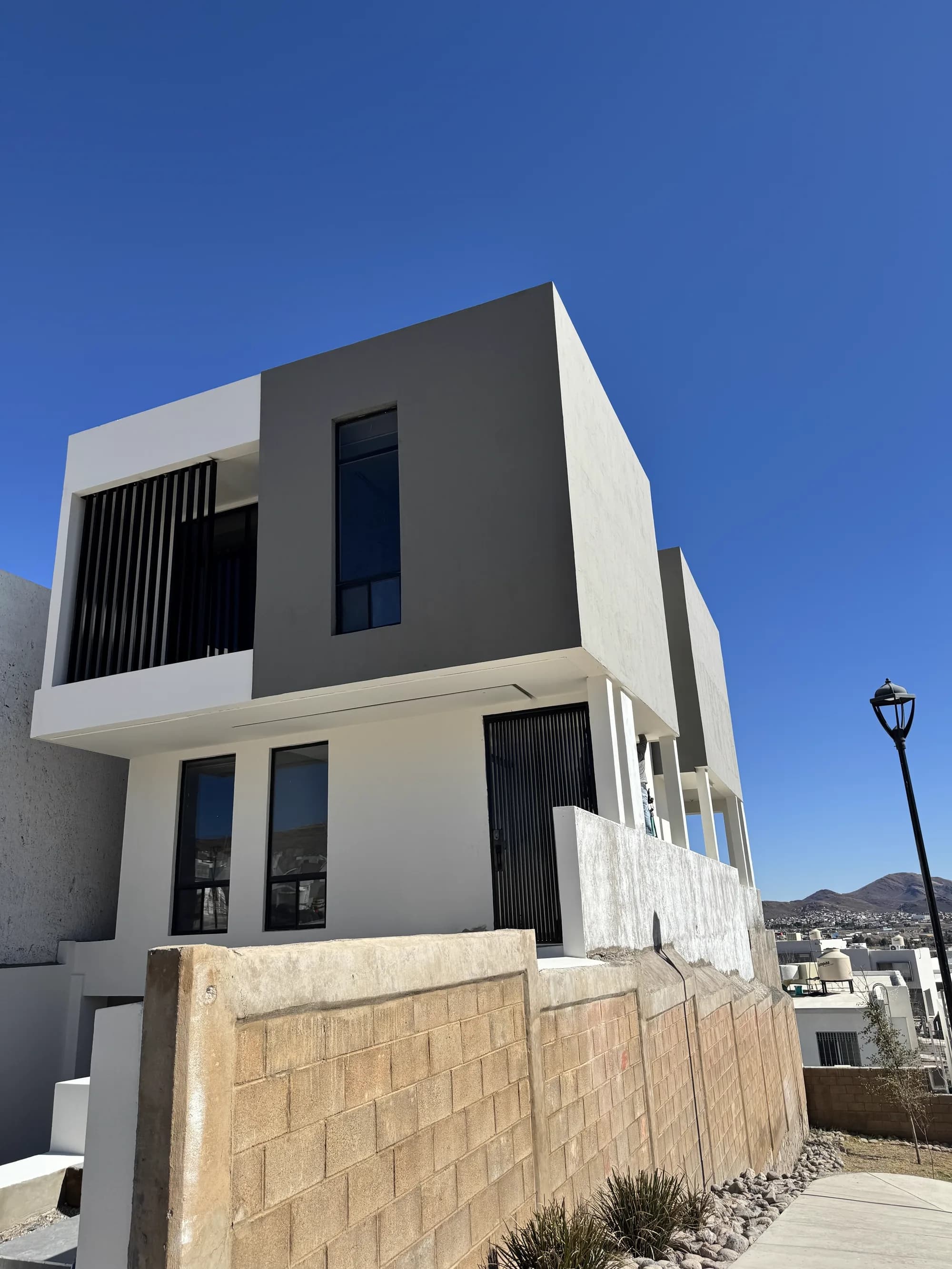 Fachada terminada de Casa Caleres, con el volumen superior en gris sobre la planta baja blanca y la celosía vertical.